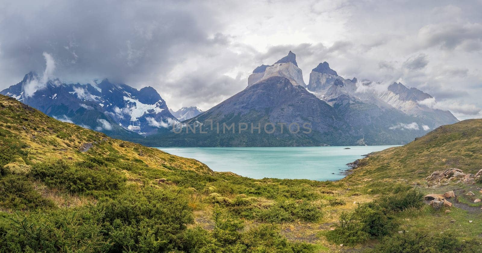 Stunning turquoise lake encircled by tall mountains and greenery in a panoramic view.