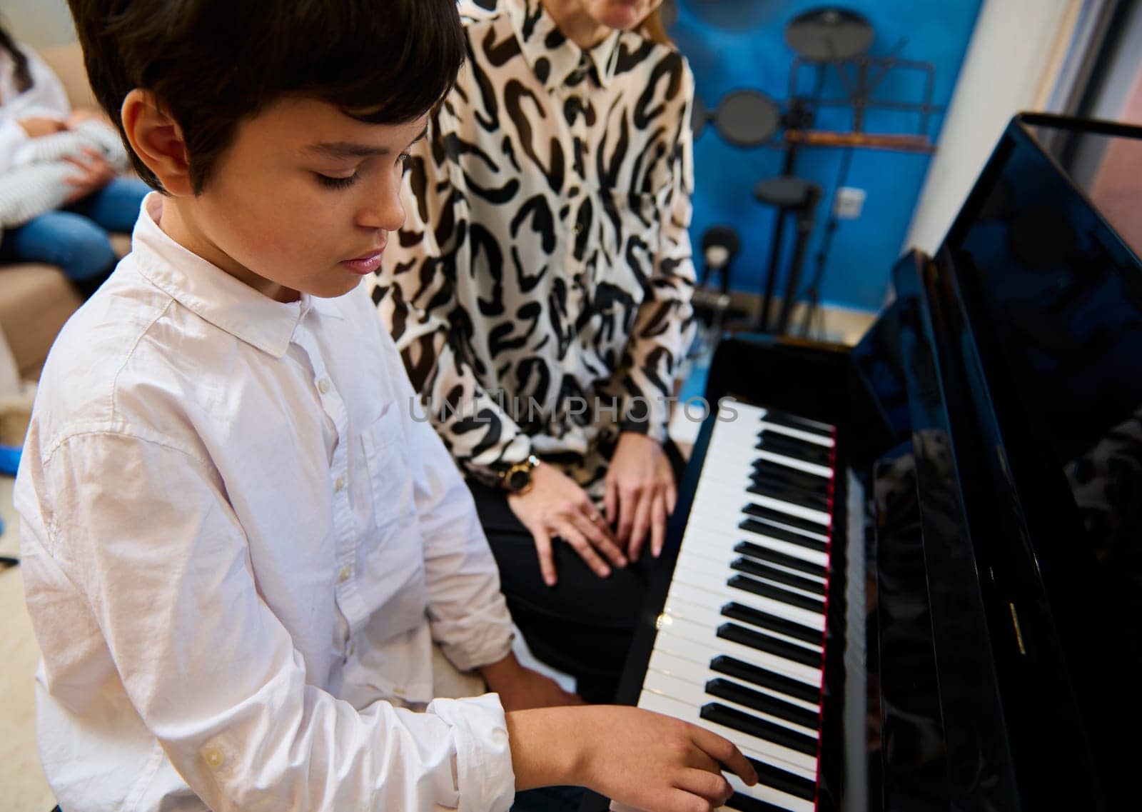 View from above of confident talented teenage musician plays piano forte, creates music and song composes a melody during music lesson. Teenager boy confidently playing grand piano during music lesson