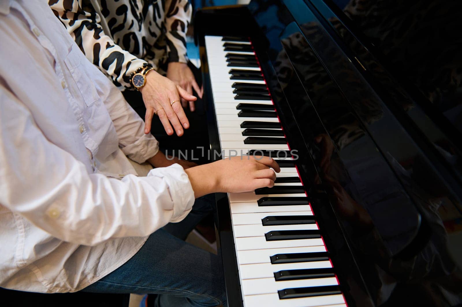 Selective focus to teenage boy musician pianist fingers and piano key to play the piano. Close-up child playing the piano during individual music lesson under his teacher's guidance by artgf