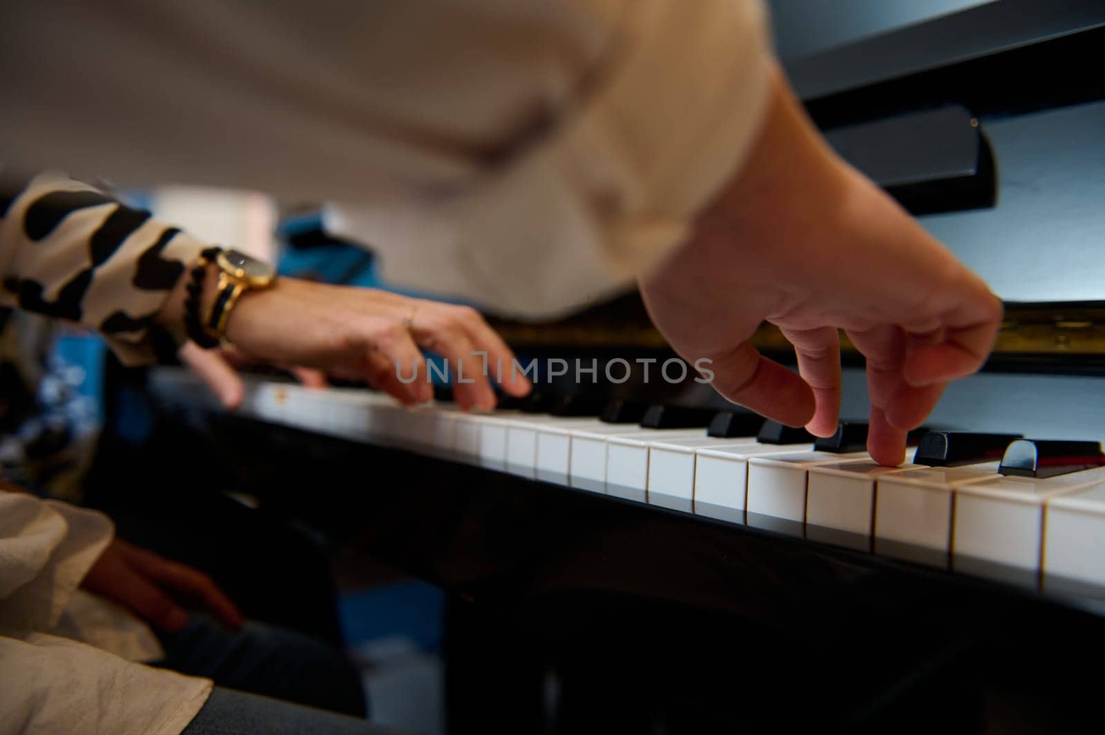 Close-up bottom view. Musician boy playing grand piano during music lesson, performing classical melody, creating and feeling the rhythm of sounds while putting fingers on white and black piano keys