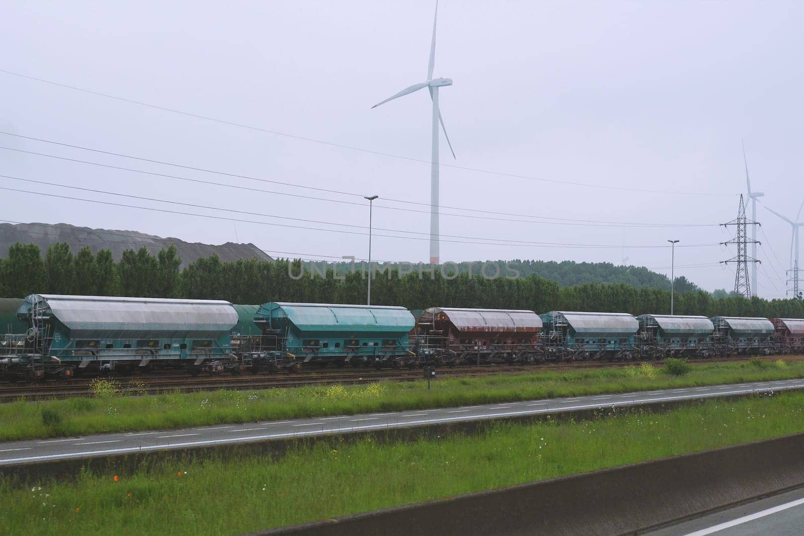 A freight train moves along the railroad tracks, passing by a bright green field on a sunny day.