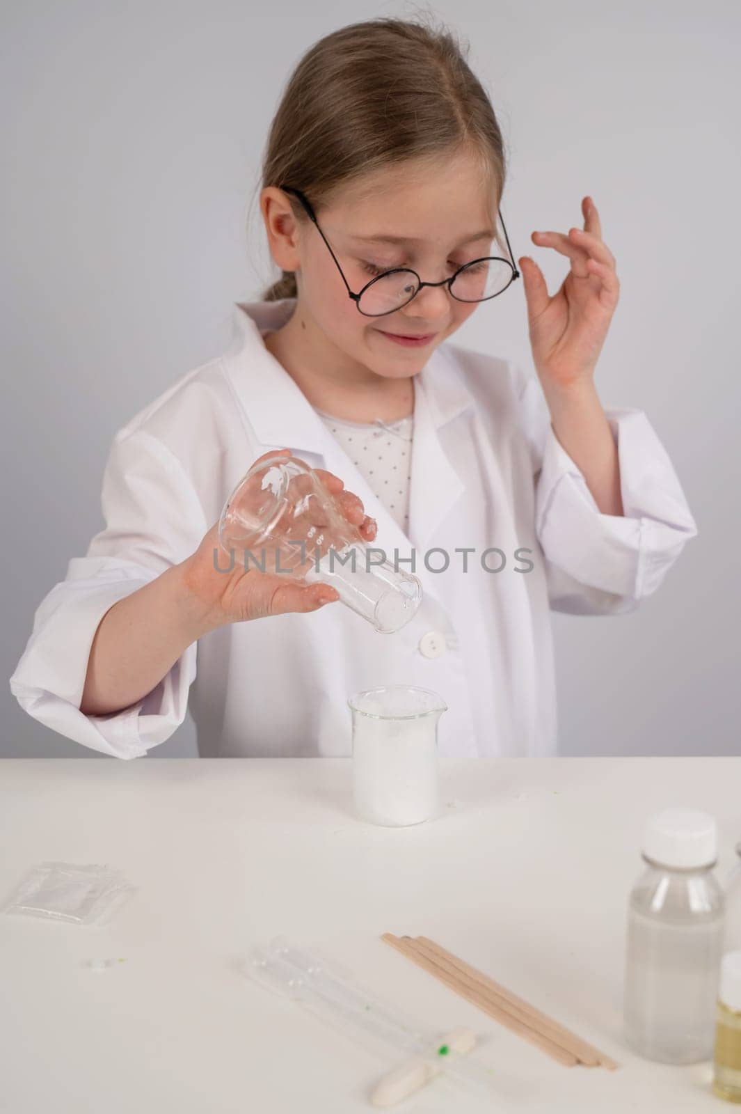 A Caucasian girl in glasses and a white coat does chemical experiments on a white background. Vertical photo. by mrwed54