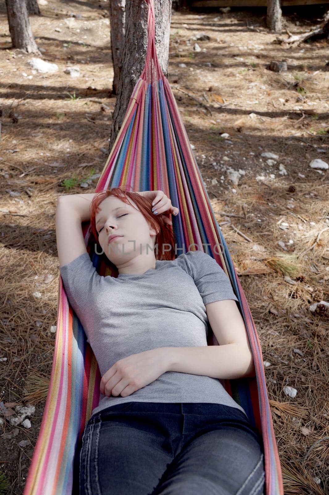 teenage girl sleeping on a hammock in the forest with her hand behind her head by Annado