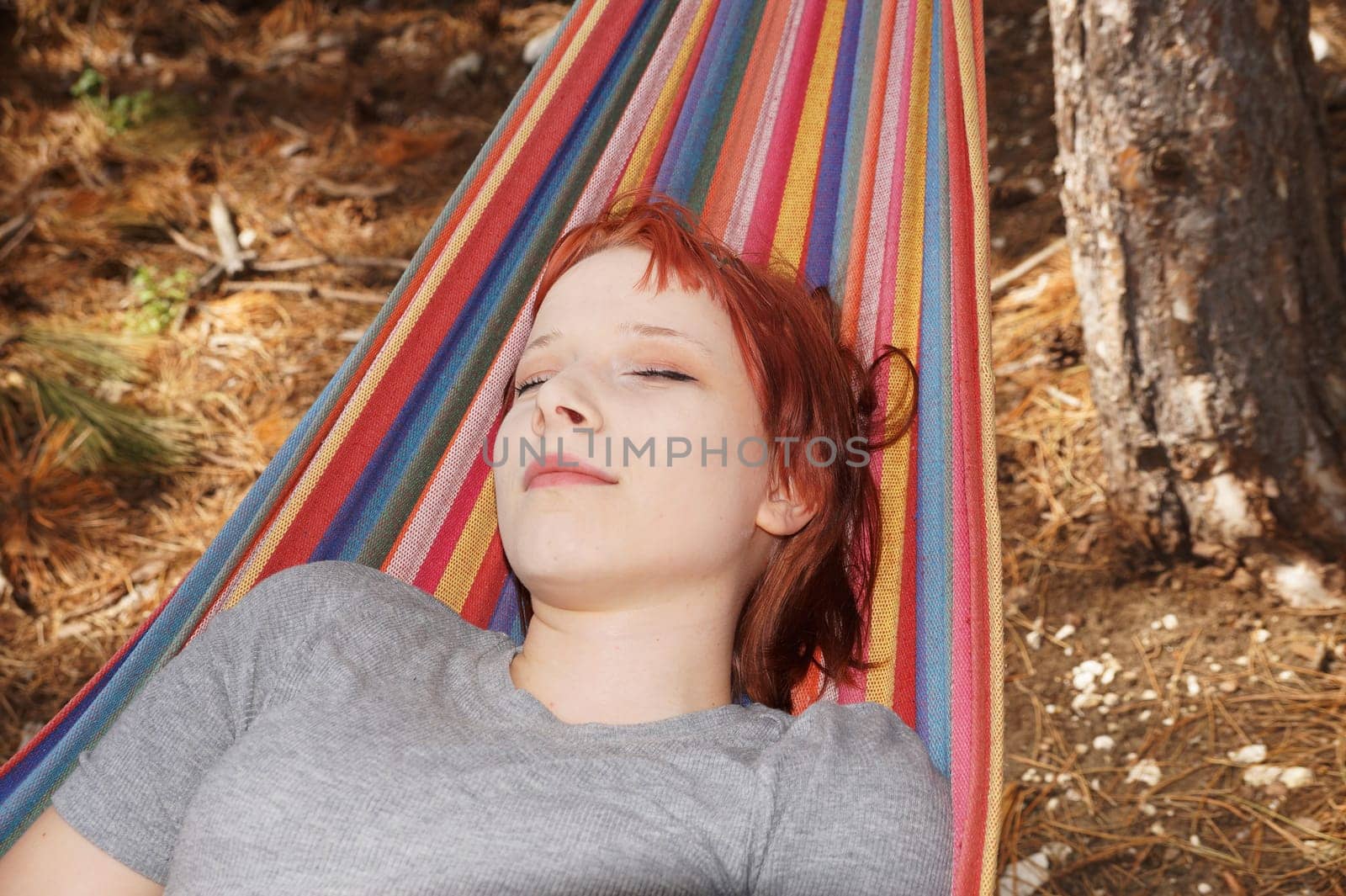 portrait of a sleeping teenage girl with red hair on a hammock in the forest.