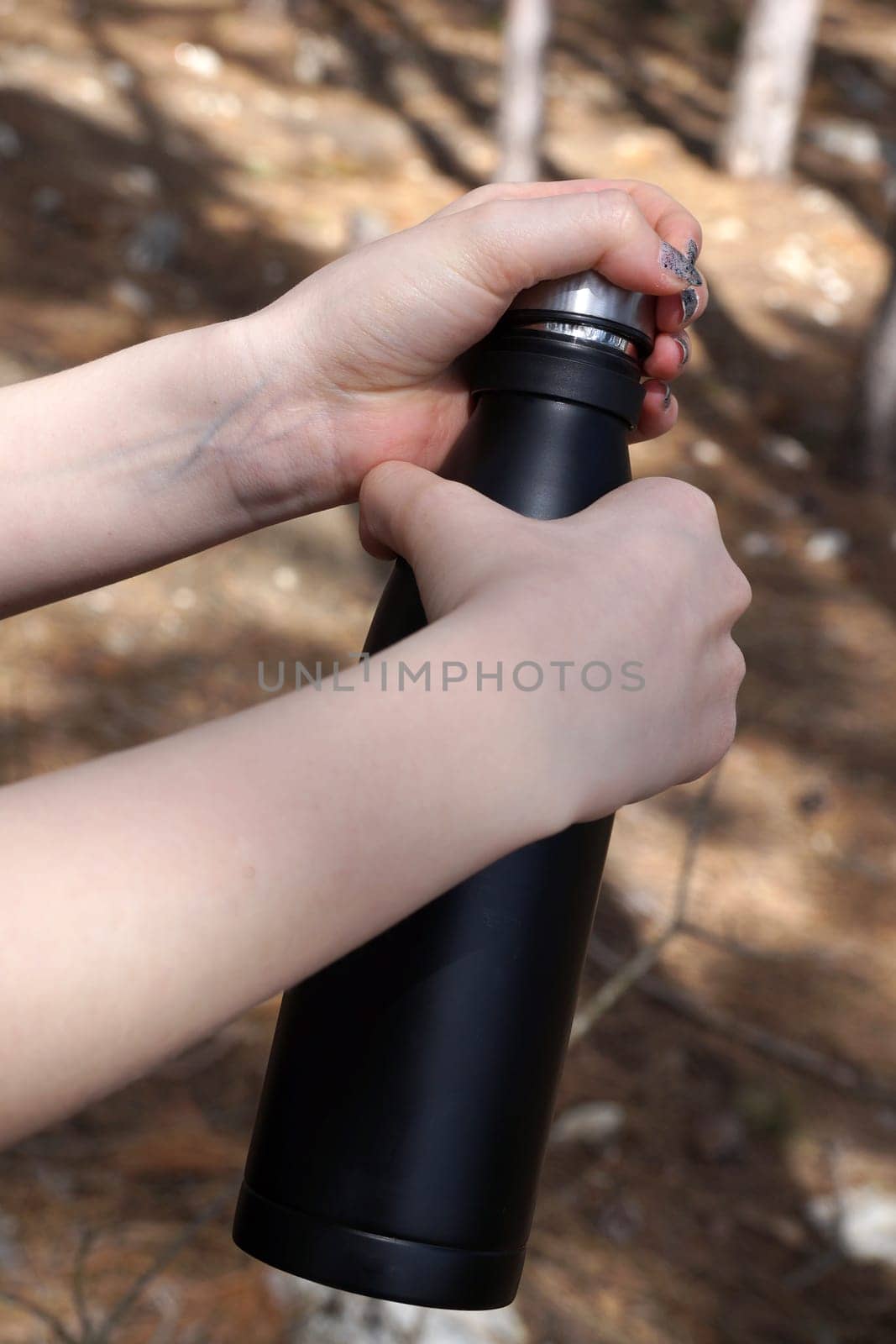 female hands open a black thermos in the forest.
