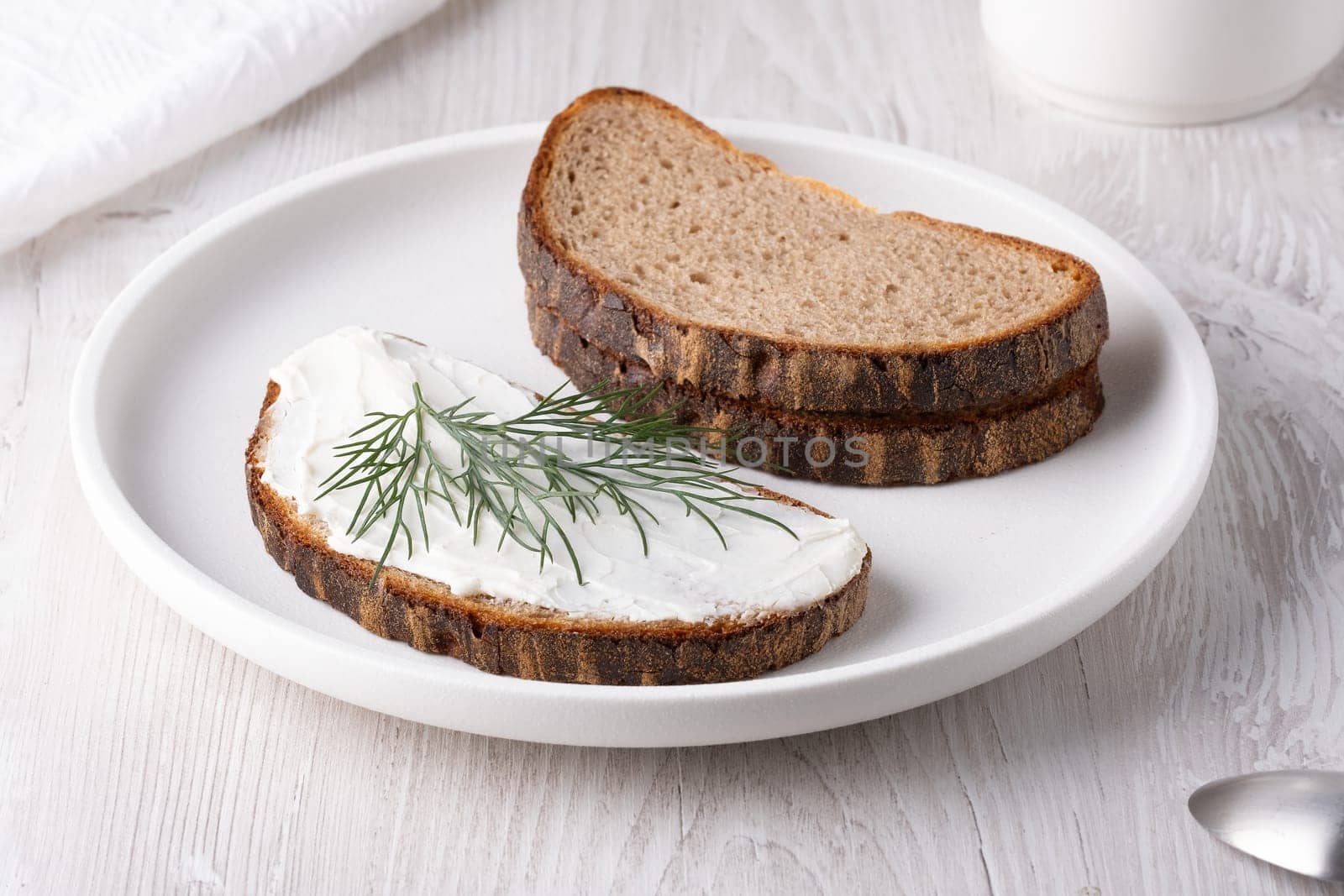 Sandwiches with soft curd cheese on a white wooden table.