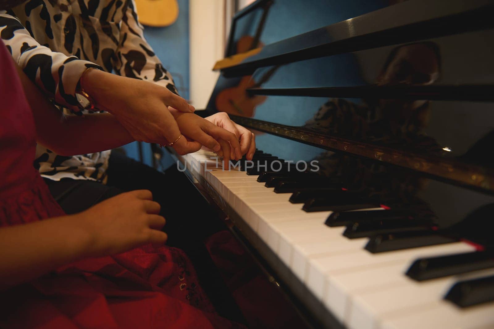 Side view of a music teacher, musician pianist holding the hands of a kid girl, teaching piano, showing the correct finger position. Hobbies and leisure. Kids education, artistic skills development