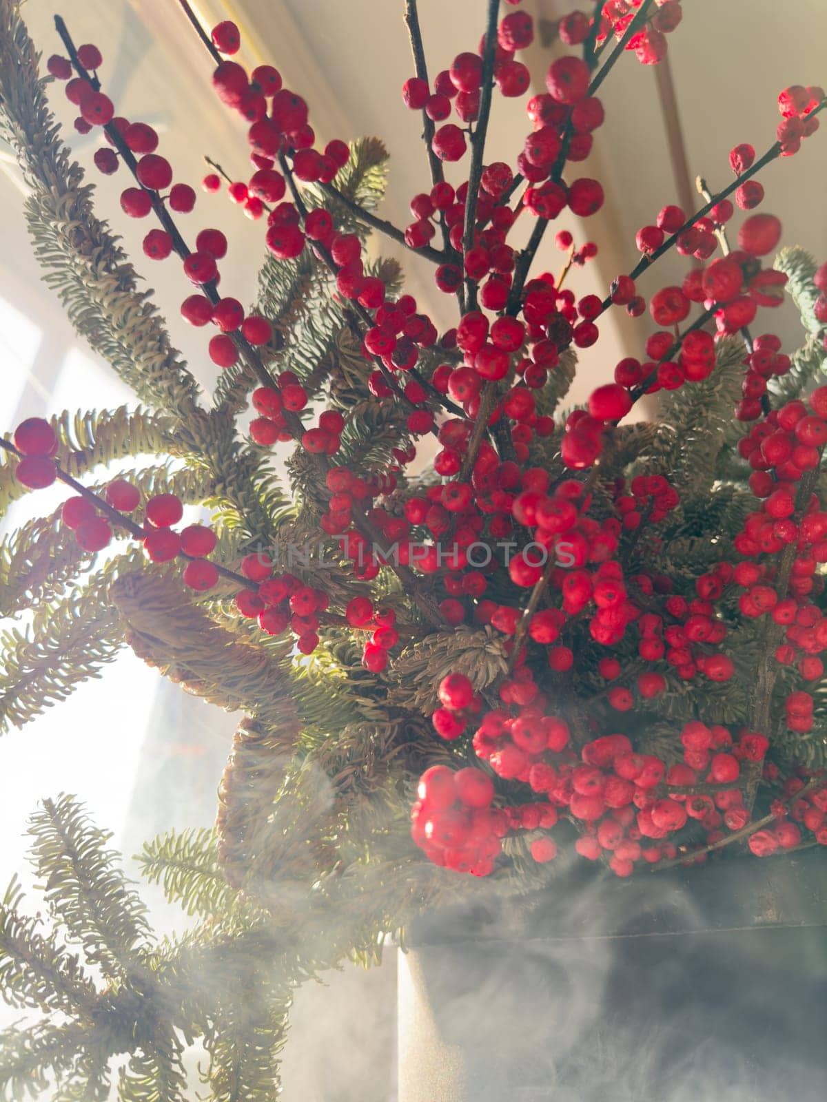 a bouquet of branches with red berries and fir branches in smoke in sunny weather, the rays of the sun through the branches. High quality photo
