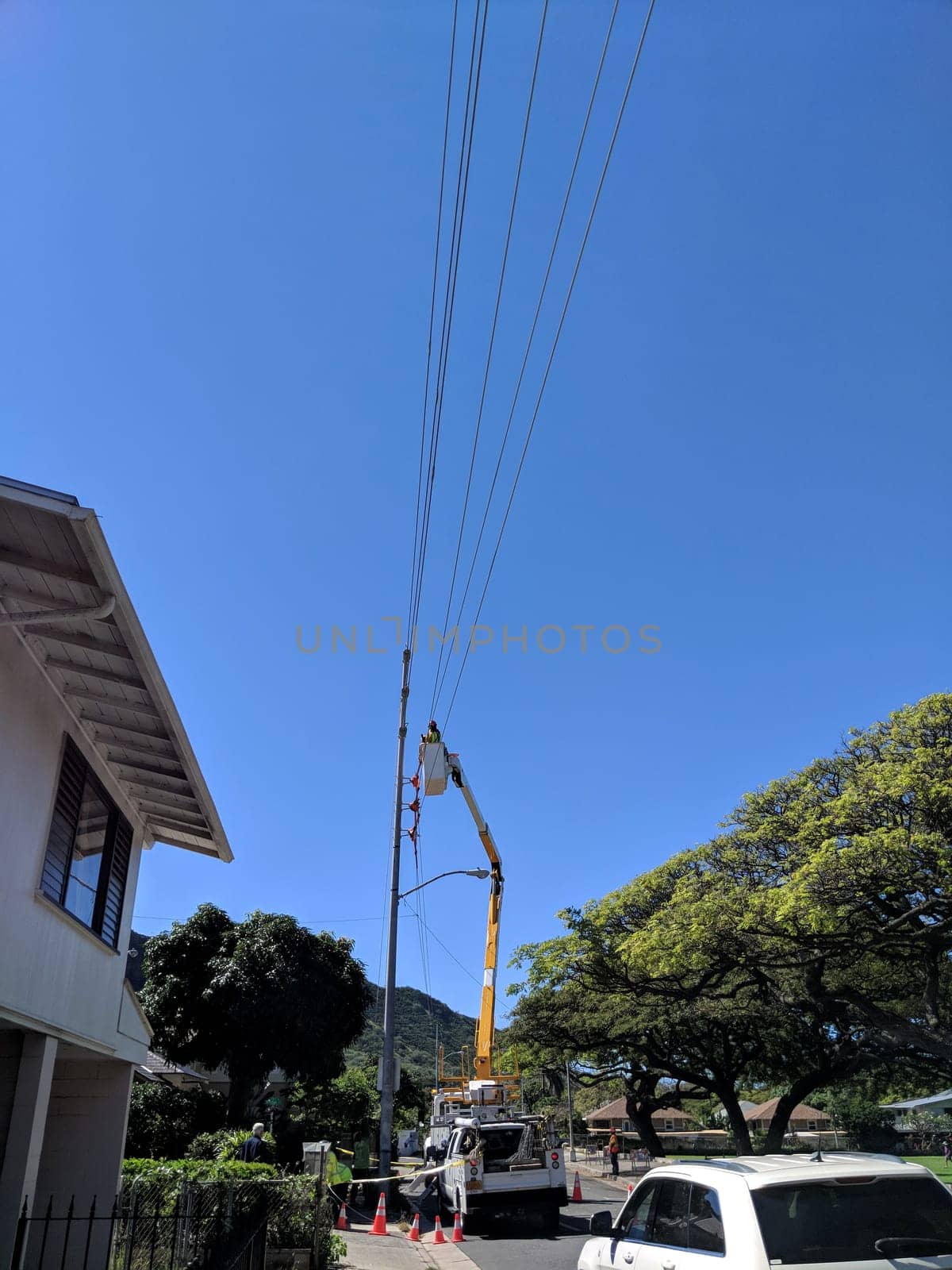 Waikiki - March 28, 2018: A skilled HECO technician ensures uninterrupted power supply by repairing a power line against the backdrop of clear blue skies and lush greenery in Waikiki.