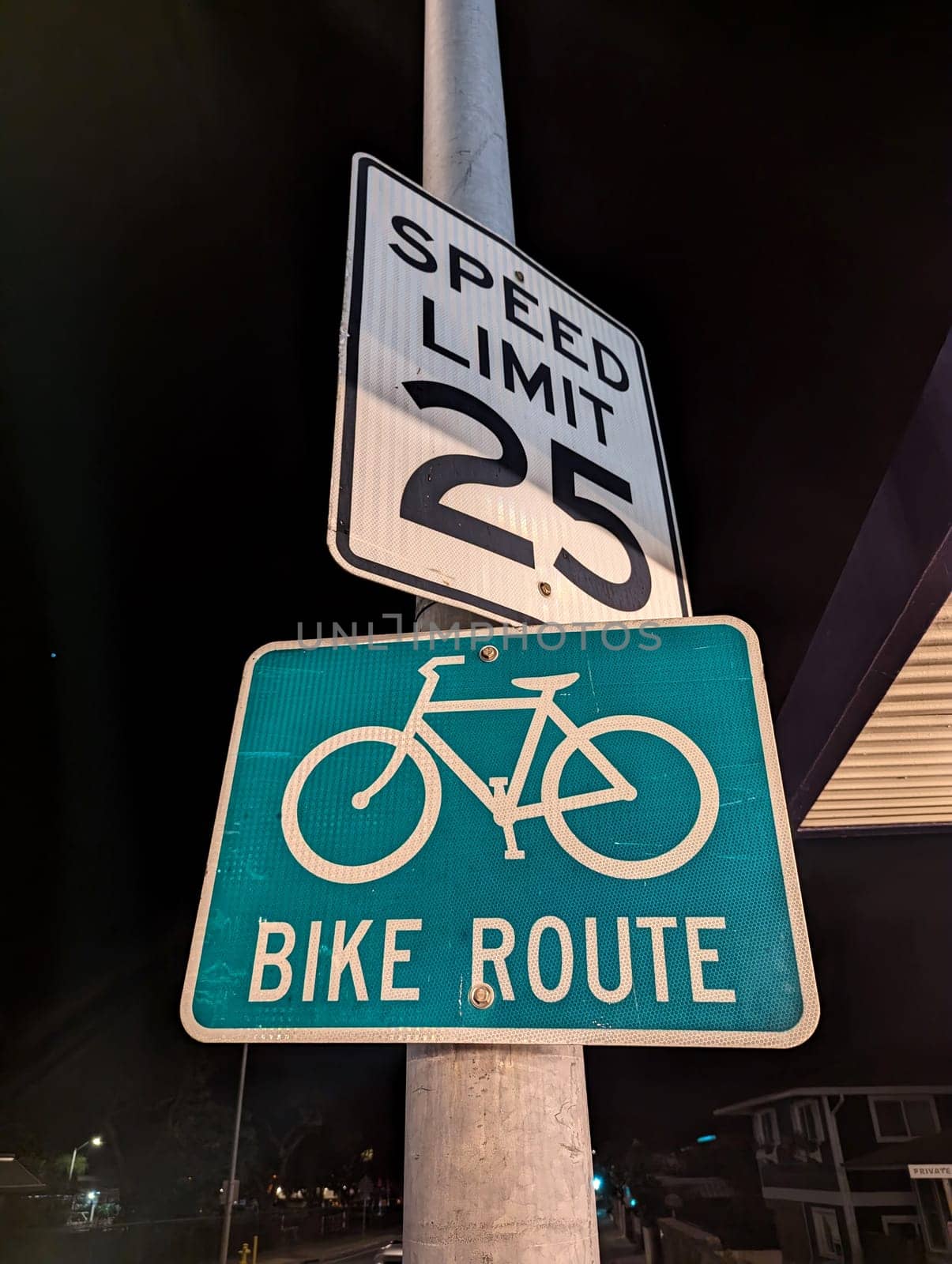Honolulu - March 21, 2023: Two essential road signs illuminated under the city lights at night. The top sign indicates a speed limit of 25, ensuring drivers maintain a safe speed, while the vibrant green sign below marks the path as a designated bike route, highlighting the city’s commitment to safety and eco-friendly transportation options.
