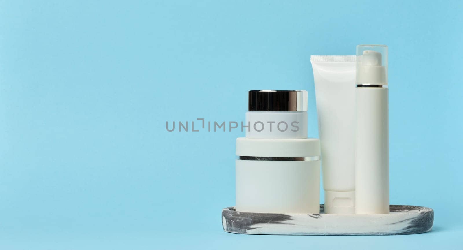 White plastic tubes, jars, and containers for cosmetic products on a blue background, copy space	