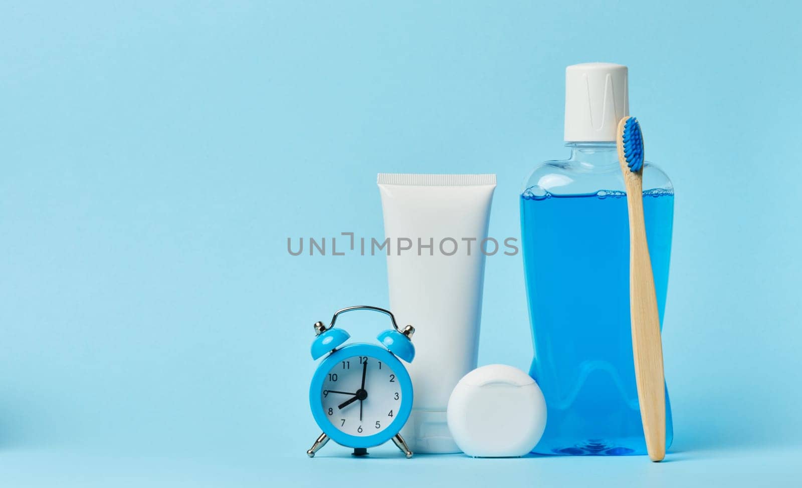 Mouthwash and toothpaste tube, alarm clock on blue background, oral hygiene
