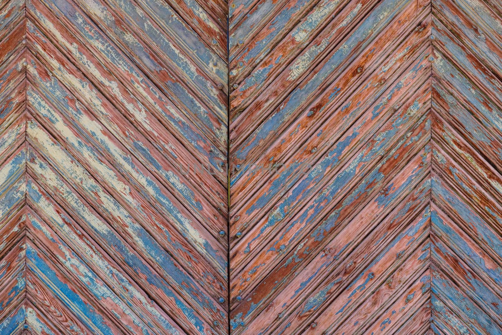 old wooden planks gate chevron pattern texture with peeled brown and blue paint layers under sun-bleached blue paint layer by z1b