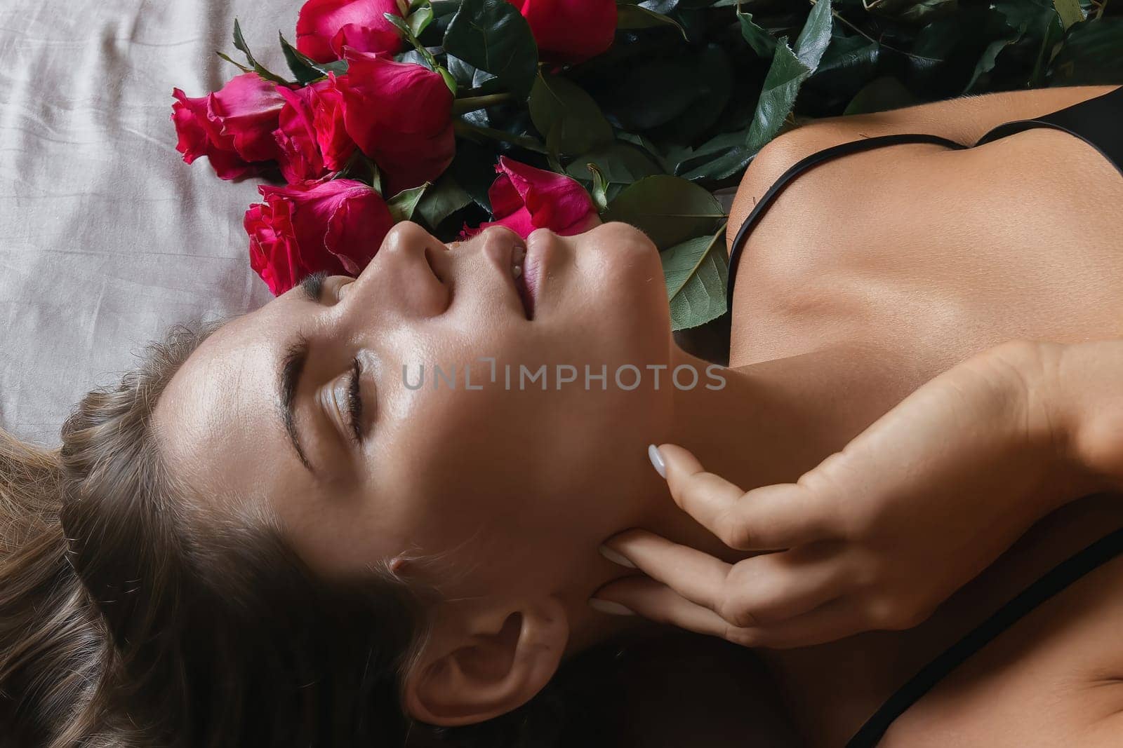 A woman is laying on a bed with a bouquet of red roses next to her. Concept of romance and intimacy, as the woman is surrounded by the flowers and he is in a relaxed and comfortable position. by Matiunina