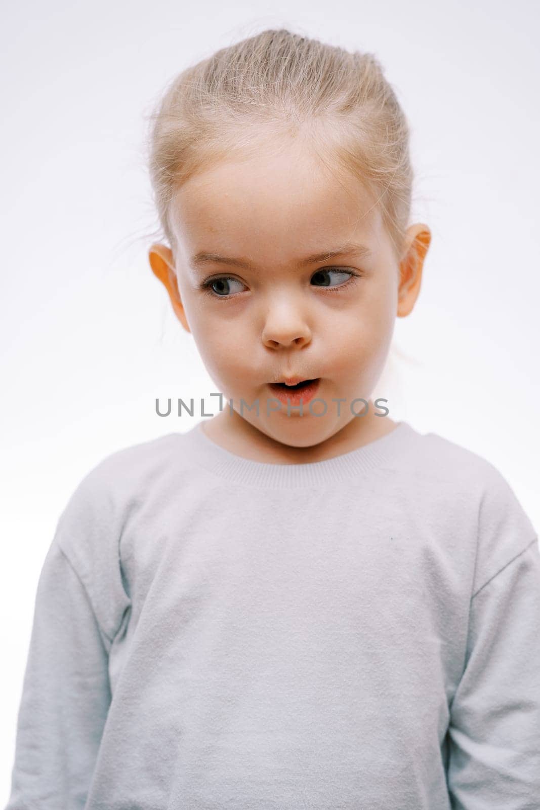 Portrait of a little surprised girl with her mouth open looking to the side on a gray background. High quality photo