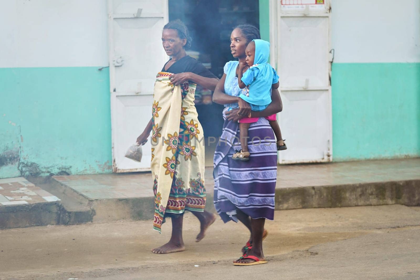 Ranohira, Madagascar - April 29, 2019: Two unknown Malagasy women walking on main street, one carrying her baby. People of Madagascar are poor but look content nevertheless
