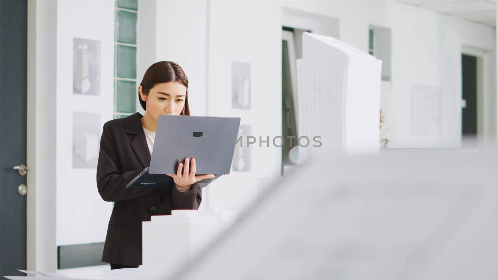 Engineer uses laptop to identify scaling features while observing 3D printed model of a building. Real estate agency worker reviewing construction scheme for new development project.