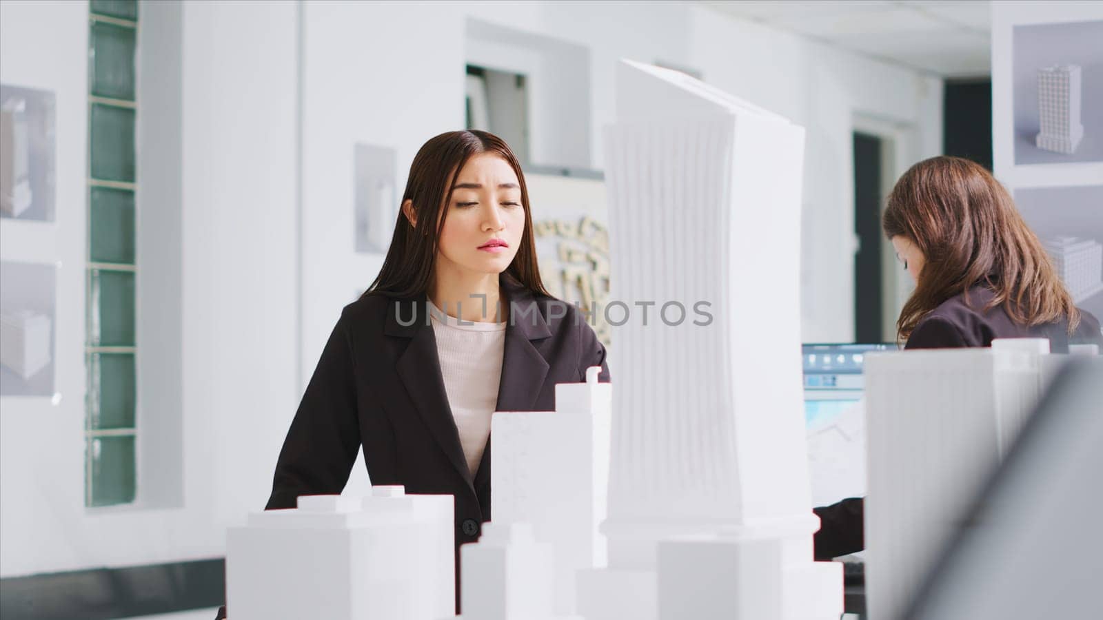 Architect analyzing blueprints and 3d building models at design table, trying to develop new industrial plan for residential area project. Woman measuring the dimensions and elements.