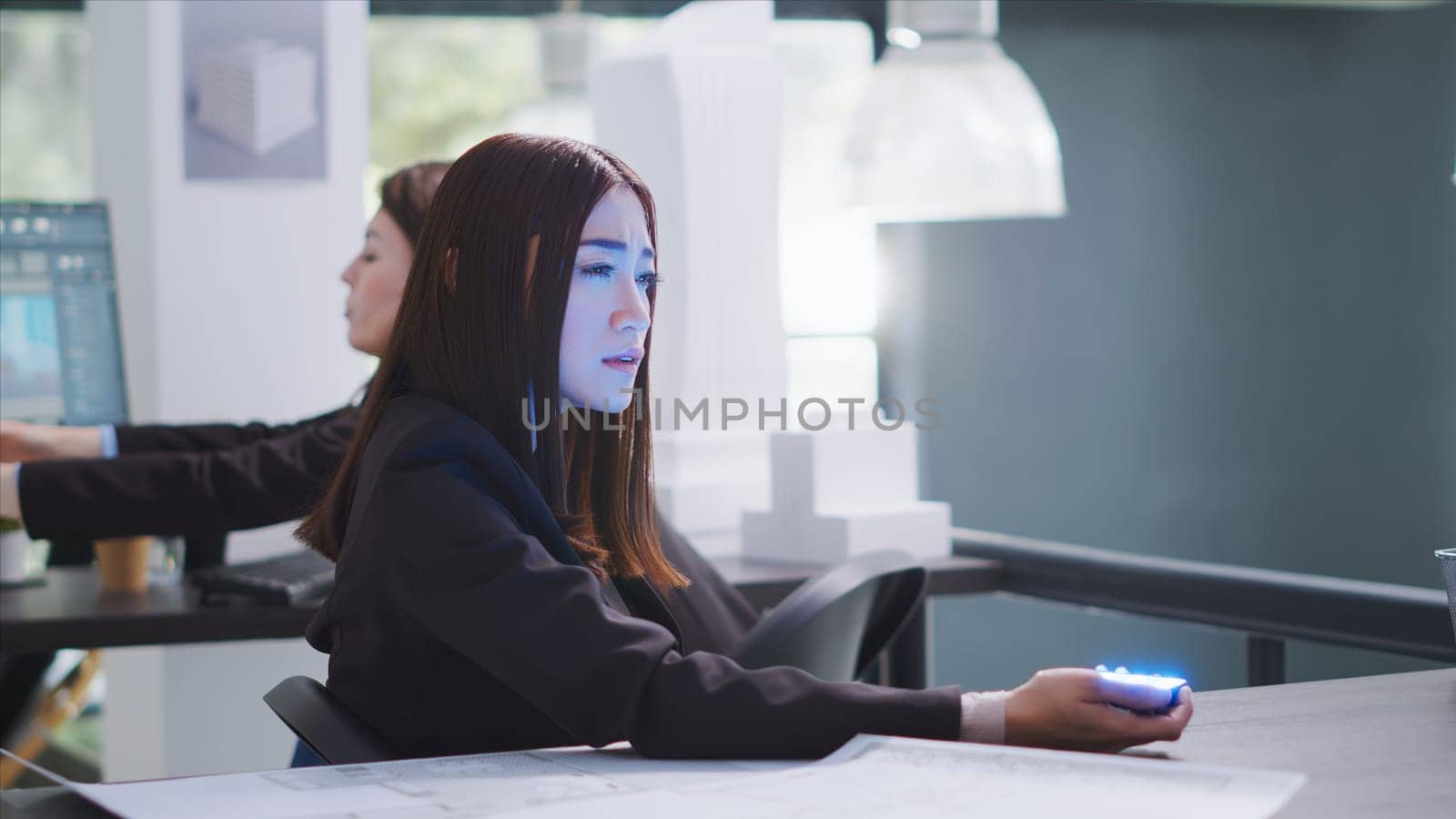 Designer speaks to advisor on projected hologram in office area, using holographic projection image to showcase engineering sketches. Workers evaluate the designing method. Tripod shot.