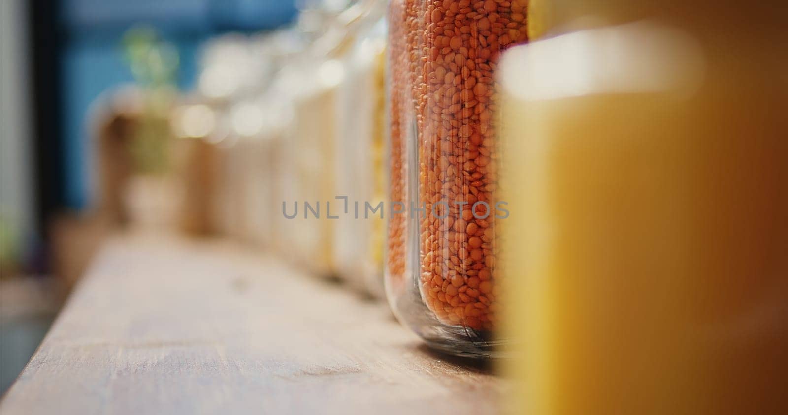 Selective focus of pasta and cereals in glass jars sold as bulk items. Homemade sauces or spices and organic farming produce placed on store shelves, nonpolluting goods. Tripod shot. Close up.