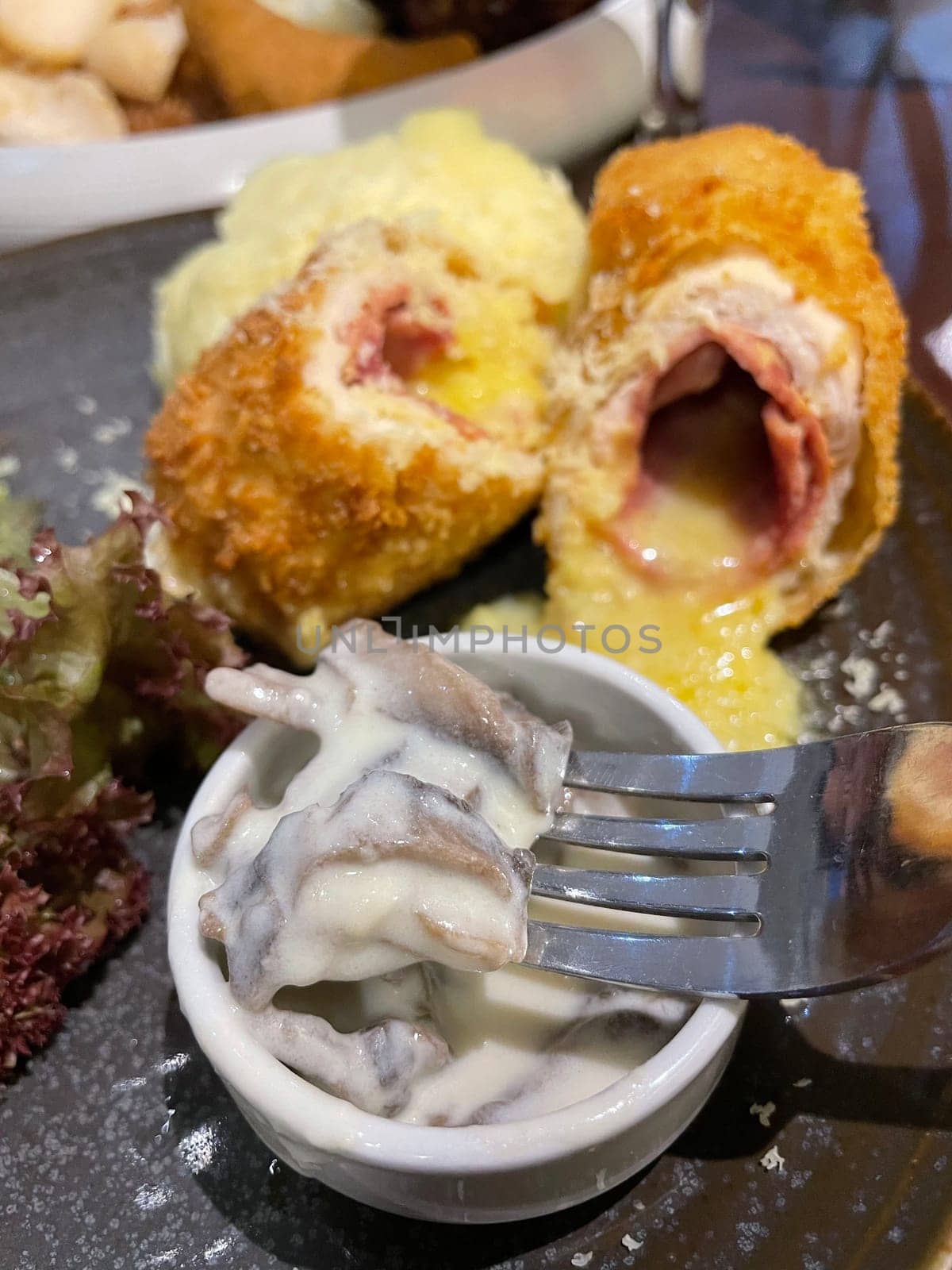 Chicken cordon bleu dish, crispy fried rolled chicken breast stuffed with cheese and ham melted in cream along with salad and mash potatoes served in brown plate