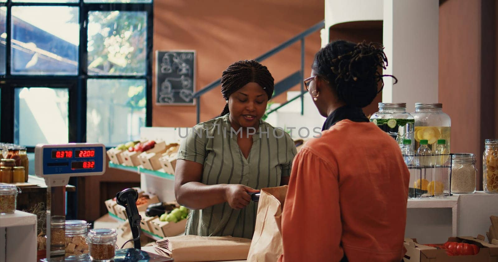 African american client paying for organic food using card, buying ethically sourced bio fruits and vegetables with pos payment at supermarket checkout. Woman purchasing produce. Handheld shot.