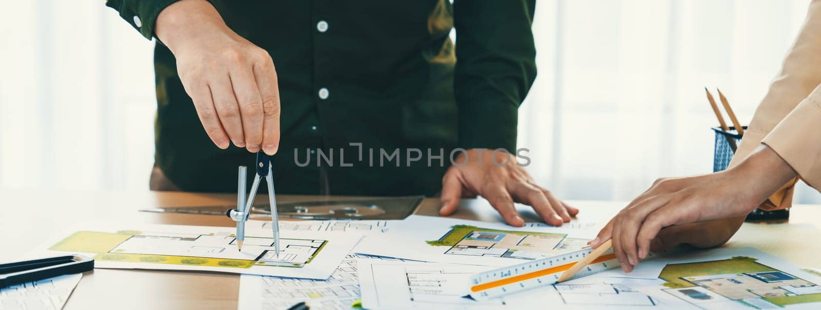 A cropped image of professional engineer using divider to measure blueprint at meeting table with blueprint, laptop and architectural equipment scatter around. Closeup. Delineation.