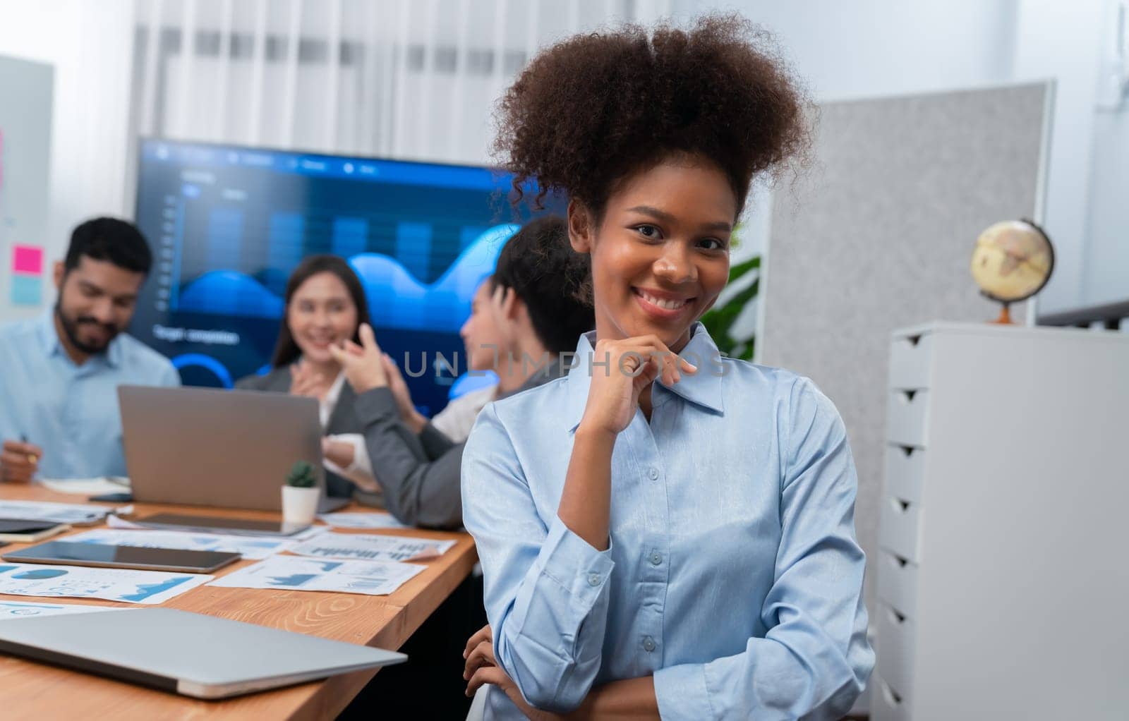 Portrait of happy young african businesswoman with group of office worker on meeting with screen display business dashboard in background. Confident office lady at team meeting. Concord