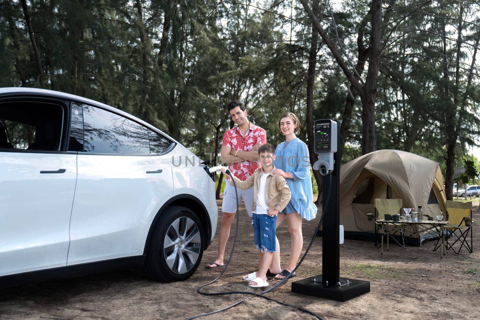 Outdoor adventure and family vacation camping in nature travel by eco friendly car for sustainable future. Lovely family recharge EV car with EV charging station in campsite. Perpetual