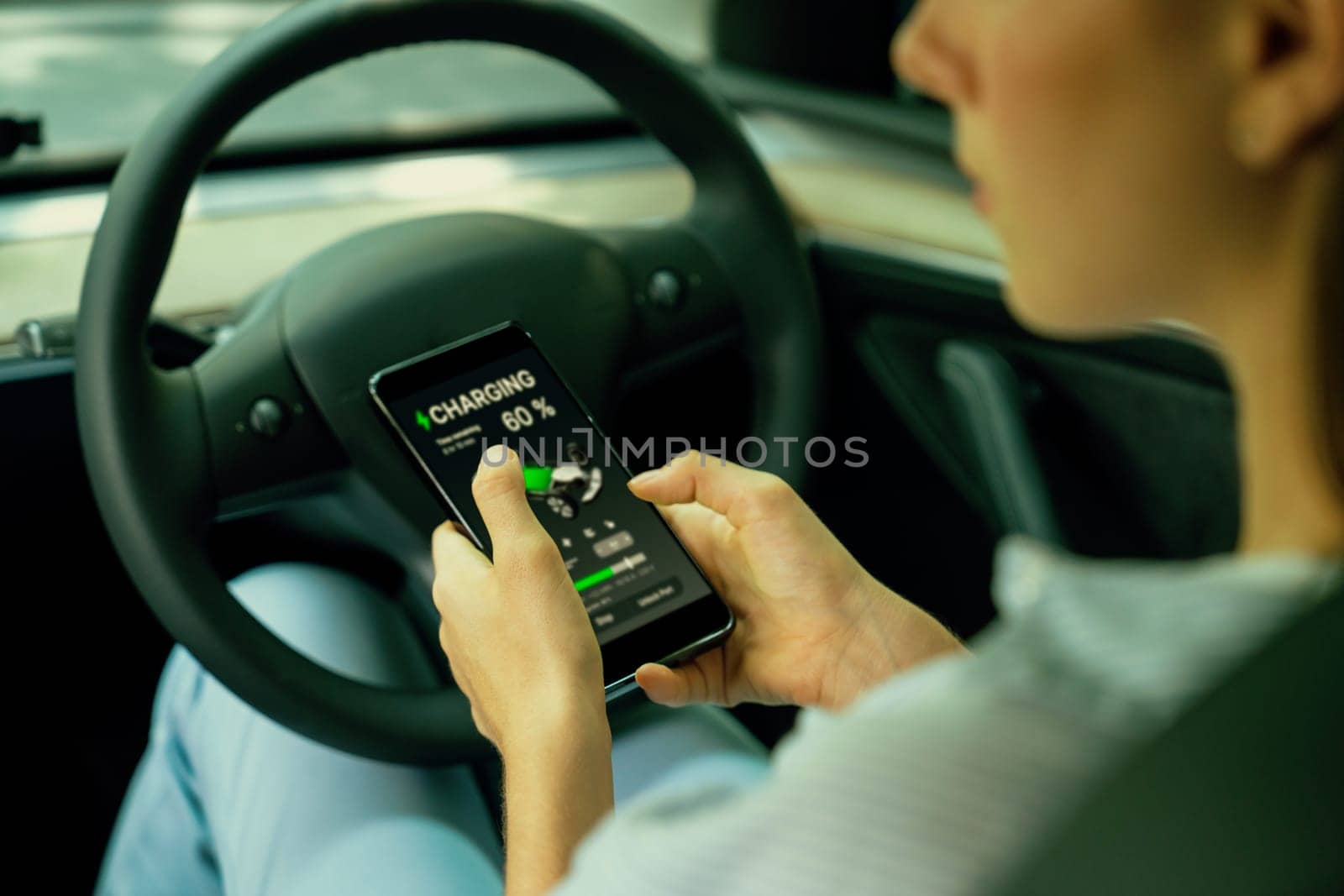 Young woman inside the vehicle, checking EV vehicle's application on battery recharging electricity status display on smartphone screen in modern EV car on her road trip journey. Exalt