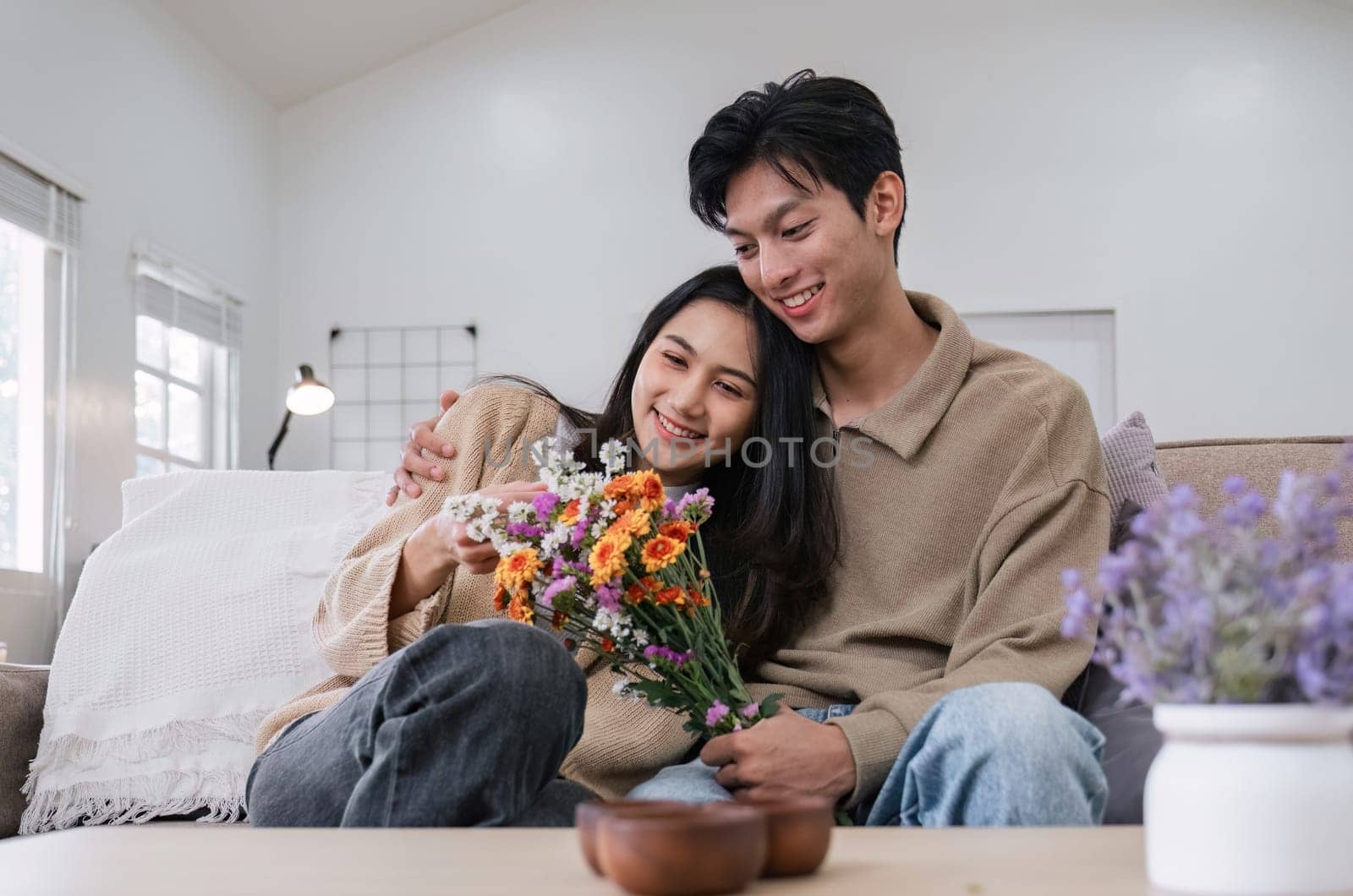 Young couple hugging and showing their love to each other. And give bouquets of flowers to each other on special days or Valentine's Day. On the sofa in the living room.