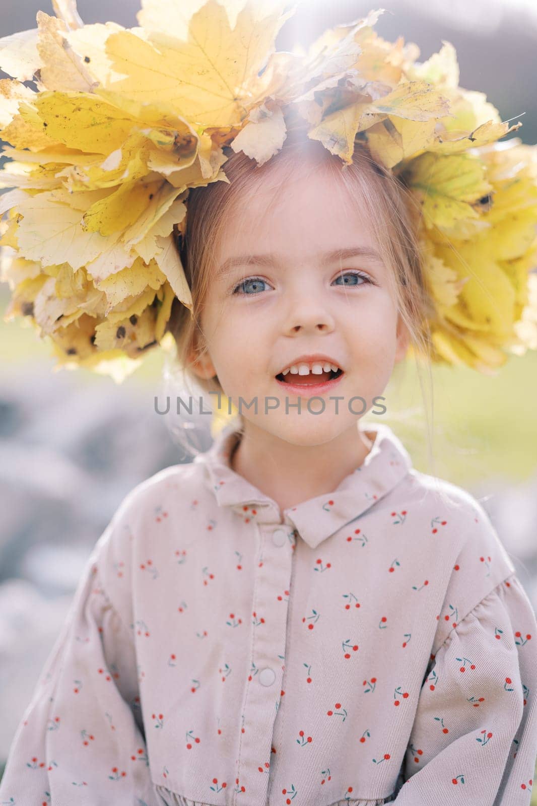 Little joyfully smiling girl wearing a wreath of yellow leaves. Portrait. High quality photo