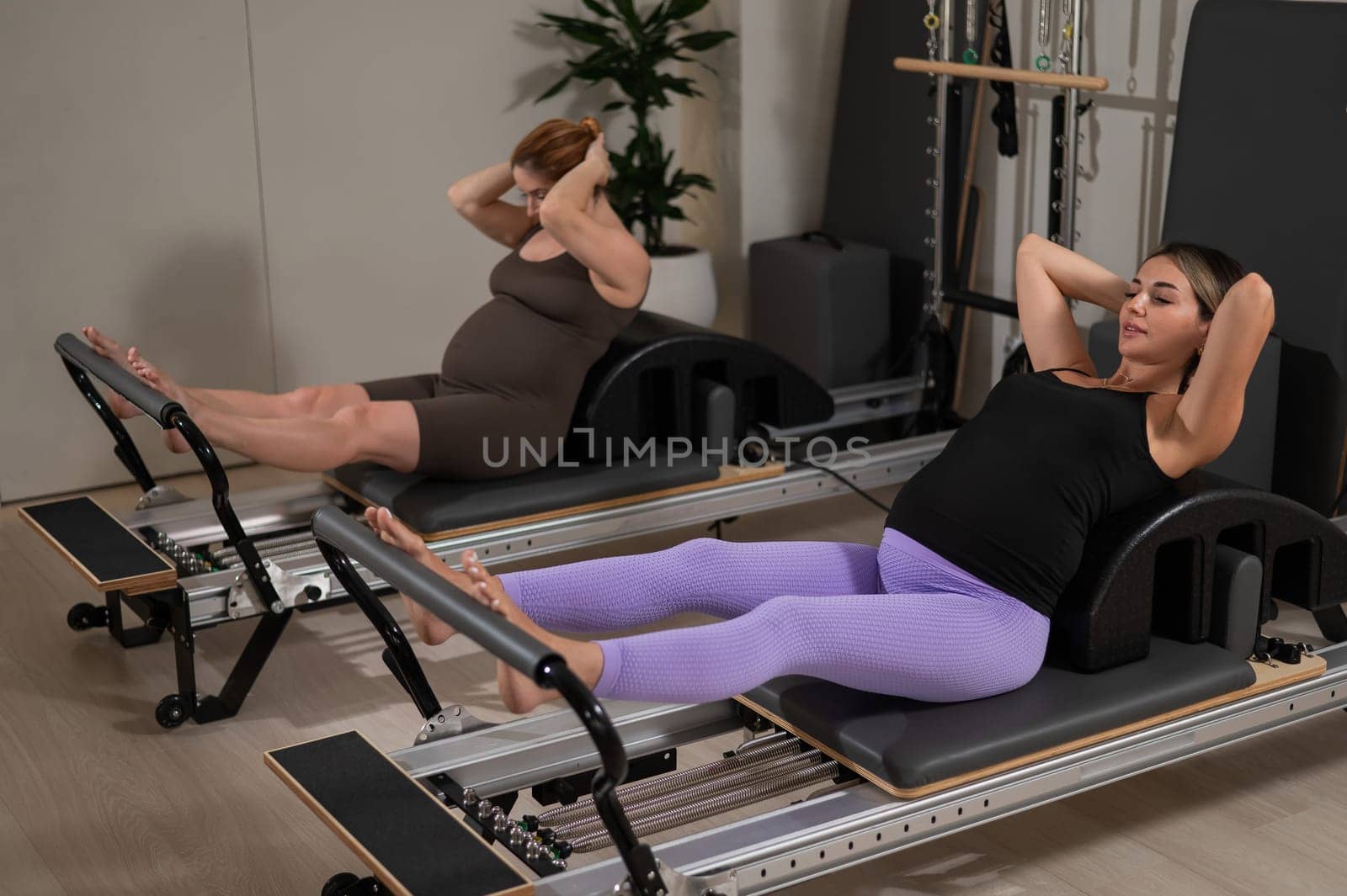 Two pregnant women do Pilates exercises on a reformer. Yoga class for pregnant women. by mrwed54
