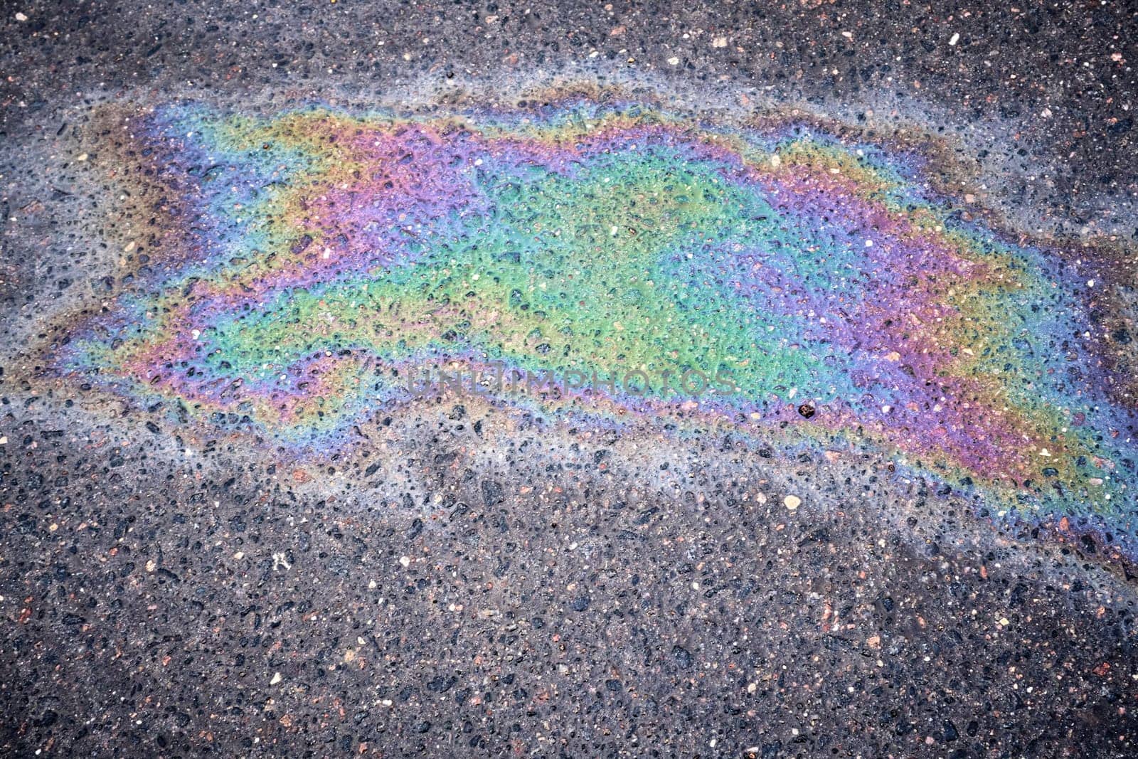 Textured stain of fuel or oil on wet asphalt during a rainy day, illustrating the concept of environmental pollution