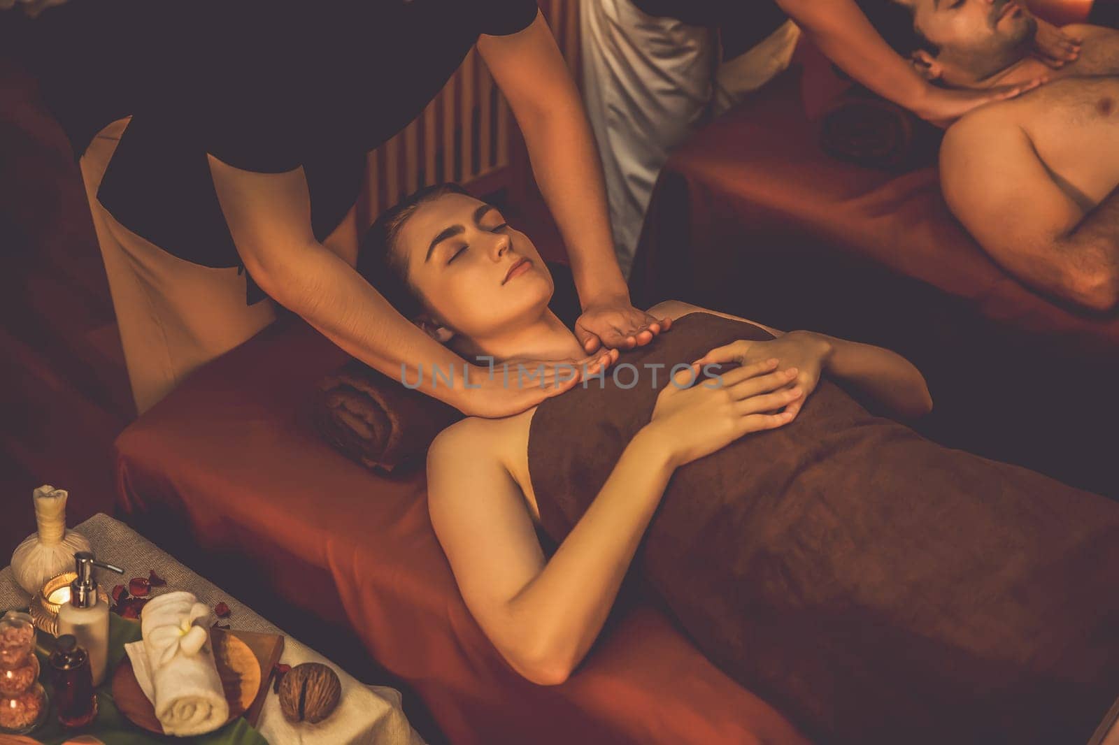 Caucasian couple customer enjoying relaxing anti-stress spa massage and pampering with beauty skin recreation leisure in warm candle lighting ambient salon spa at luxury resort or hotel. Quiescent