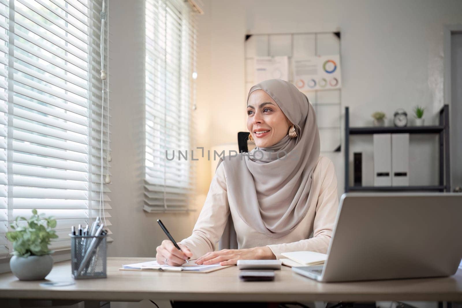Attractive Muslim accounting business woman working using laptop in modern office by wichayada