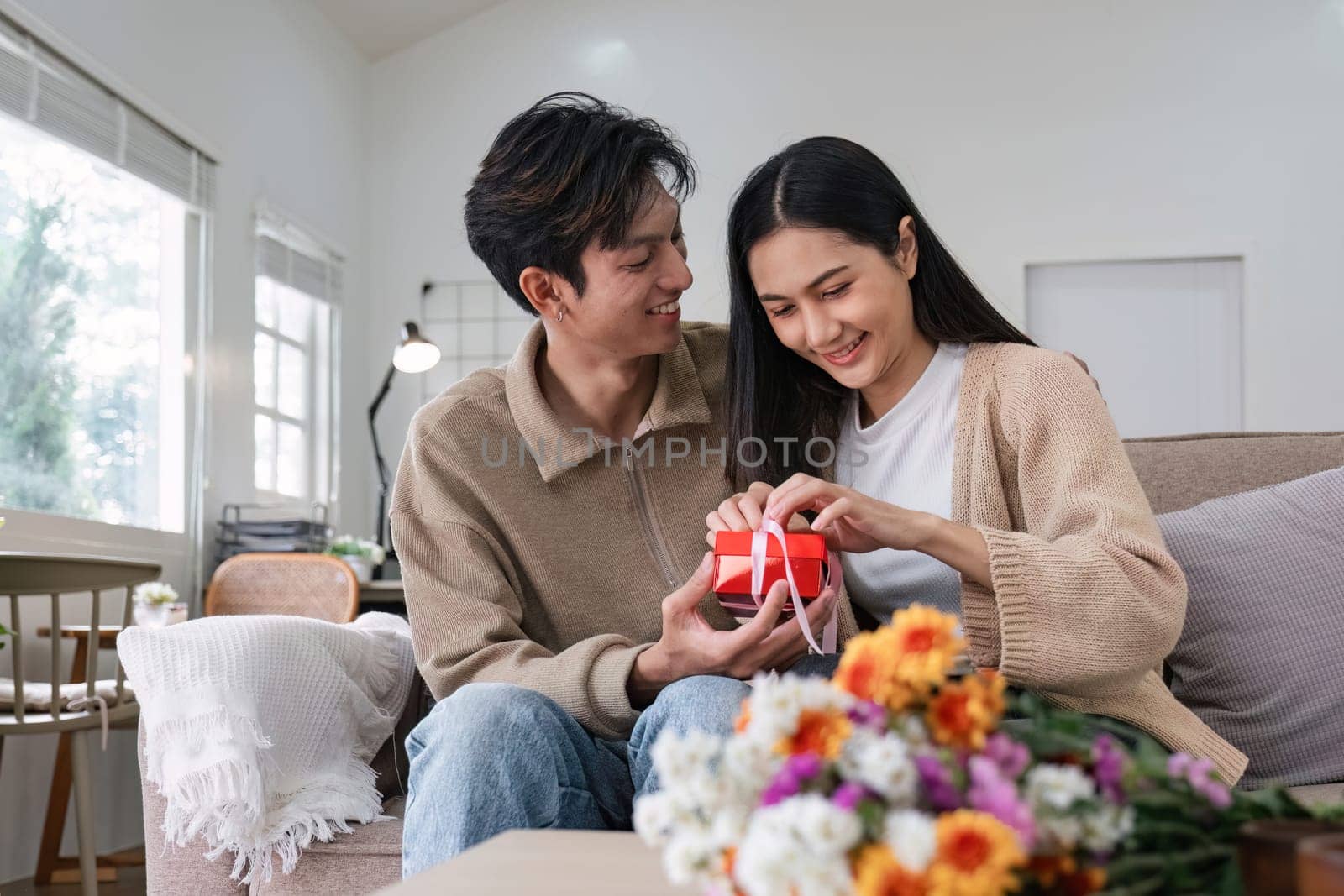 Young Asian couple giving each other giftbox on a special day. Sitting together happily in the living room.