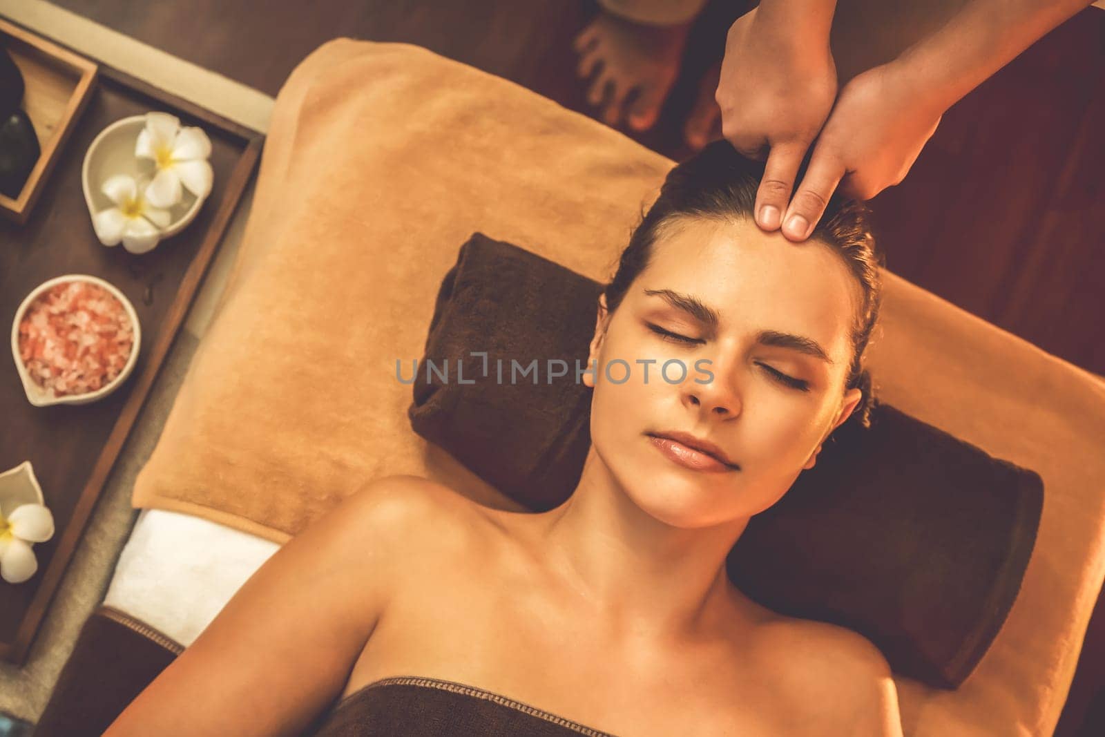 Caucasian woman enjoying relaxing anti-stress head massage and pampering facial beauty skin recreation leisure in warm candle lighting ambient salon spa in luxury resort or hotel. Quiescent