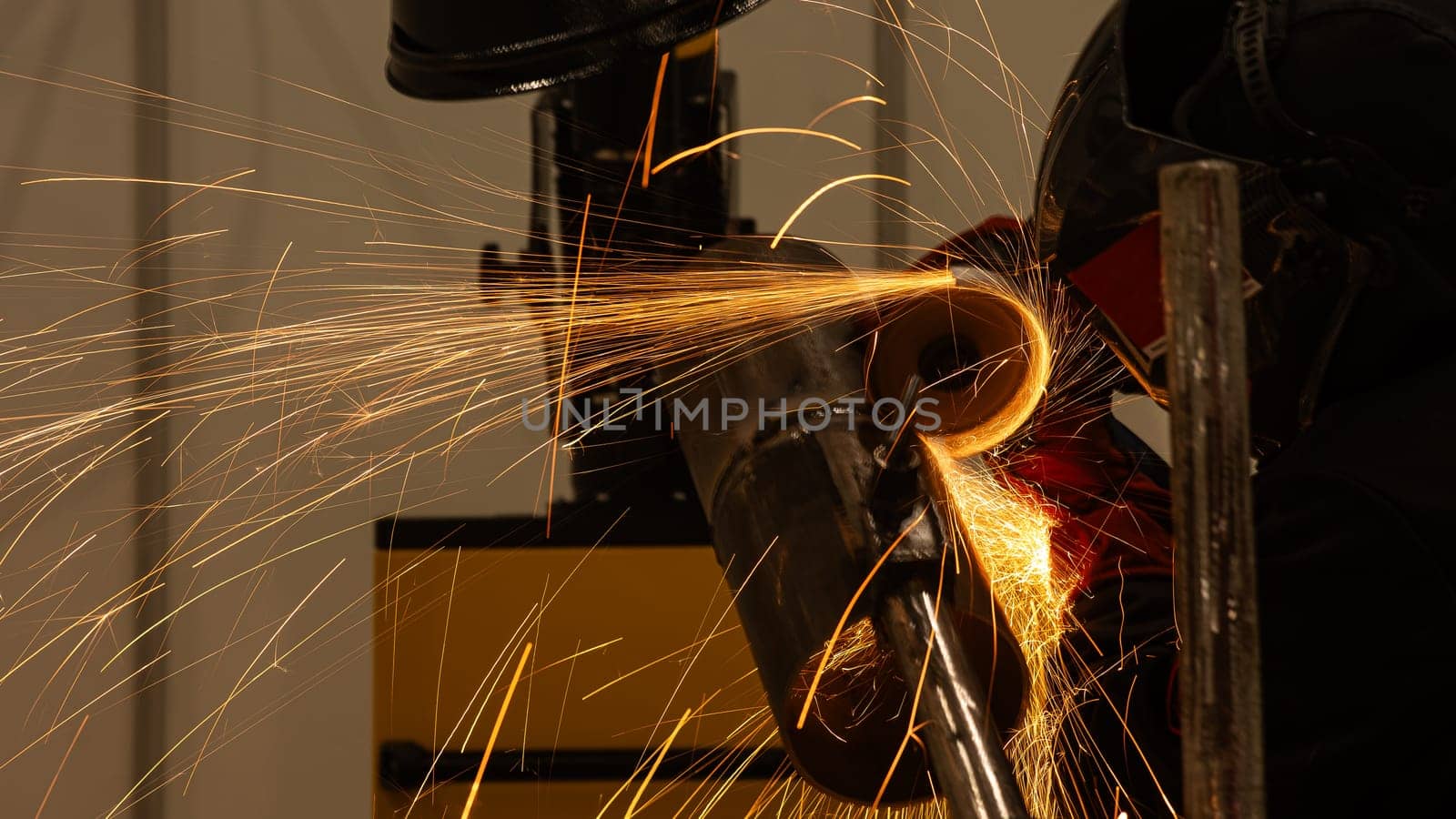 A welder wearing a protective mask cuts a metal pipe