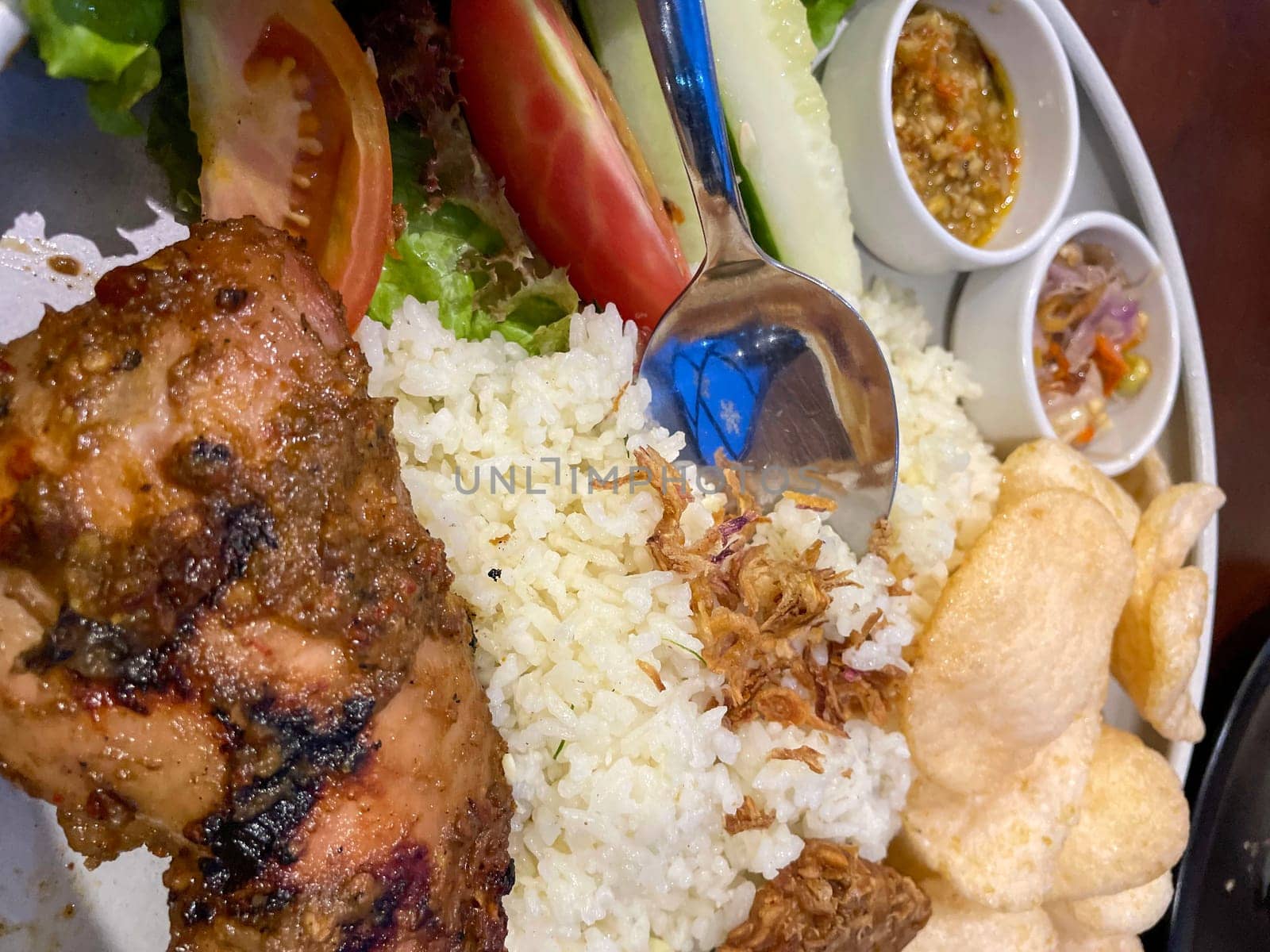 Nasi uduk ayam bakar, or coconut milk flavor rice served with grilled chicken, fresh salad, and chili paste traditional Indonesian food, indonesian street food, homemade food