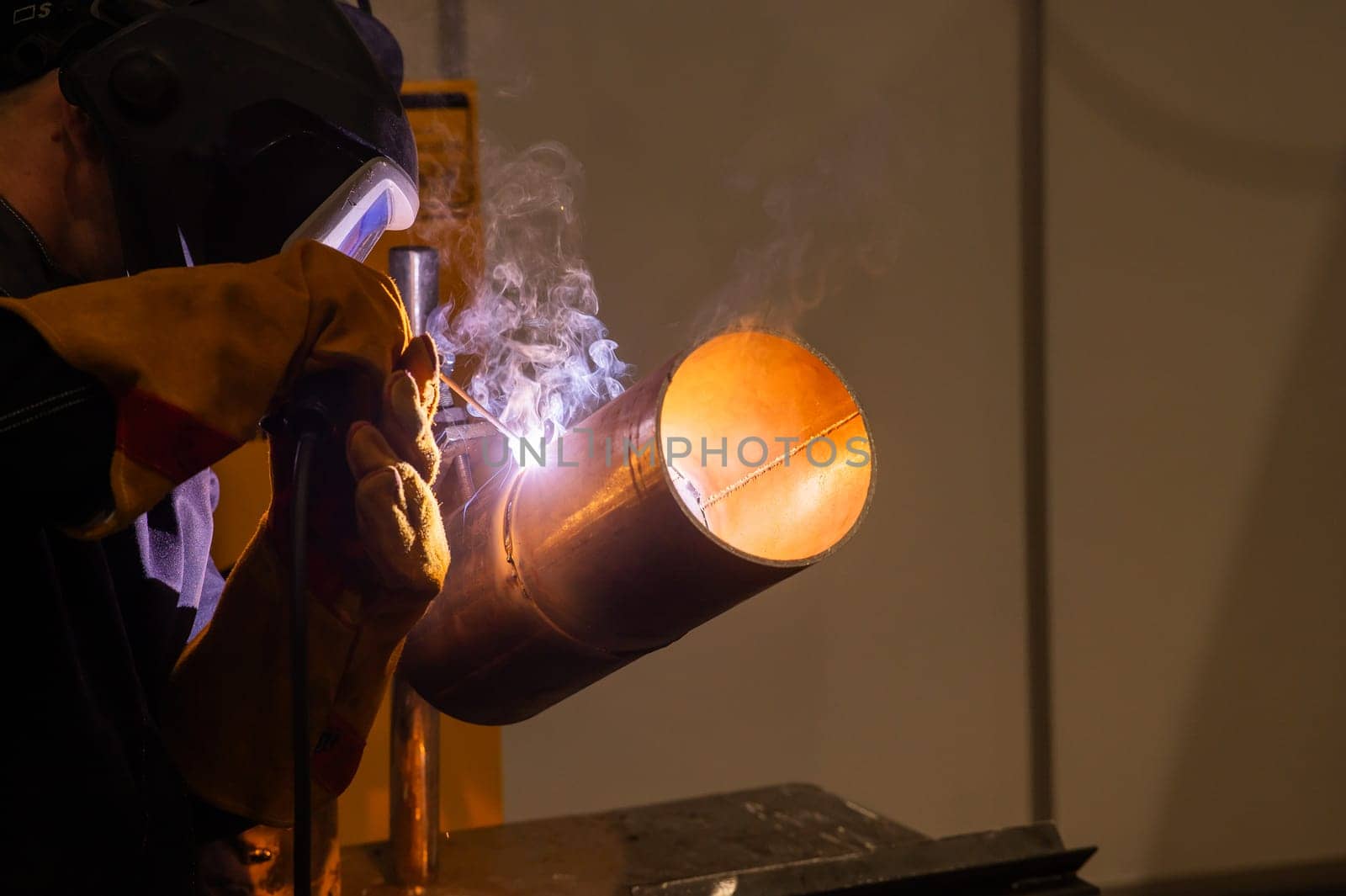 A man wearing a protective mask welds a metal pipe. by mrwed54