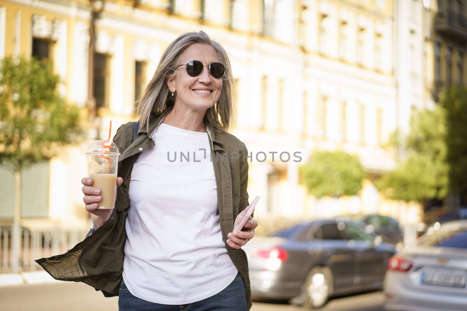 A woman strolling along a busy street while carrying a beverage in her hand.