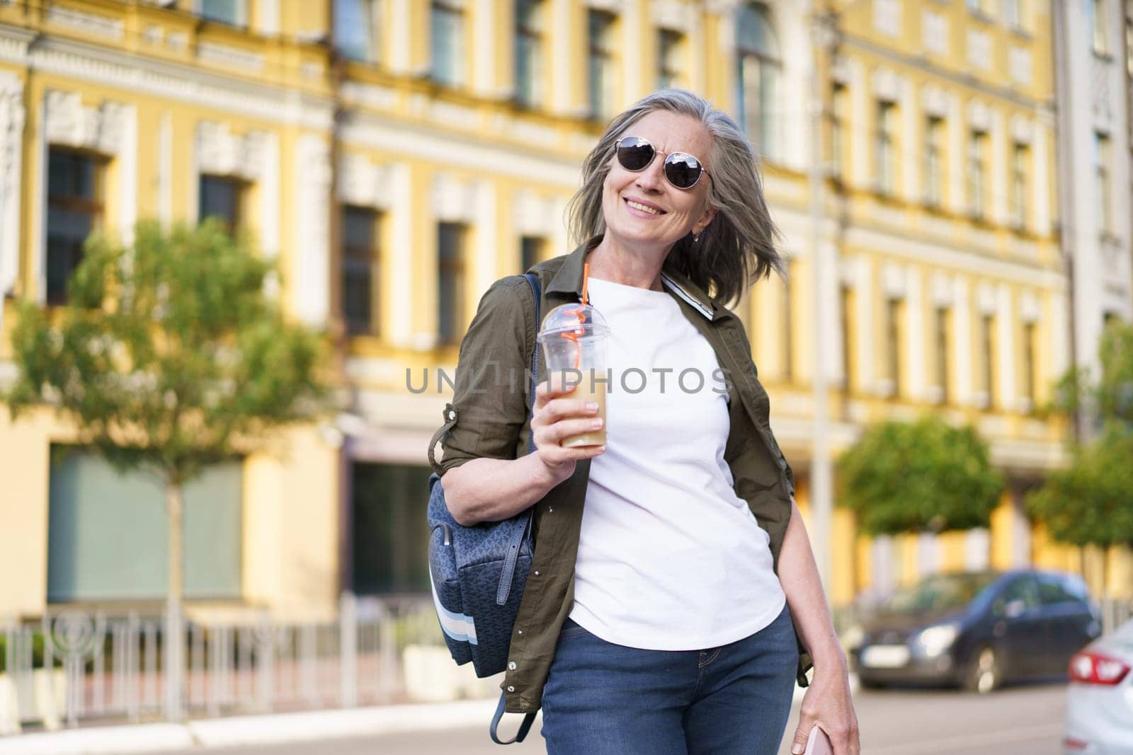 Woman Walking Down Street With Drink by LipikStockMedia