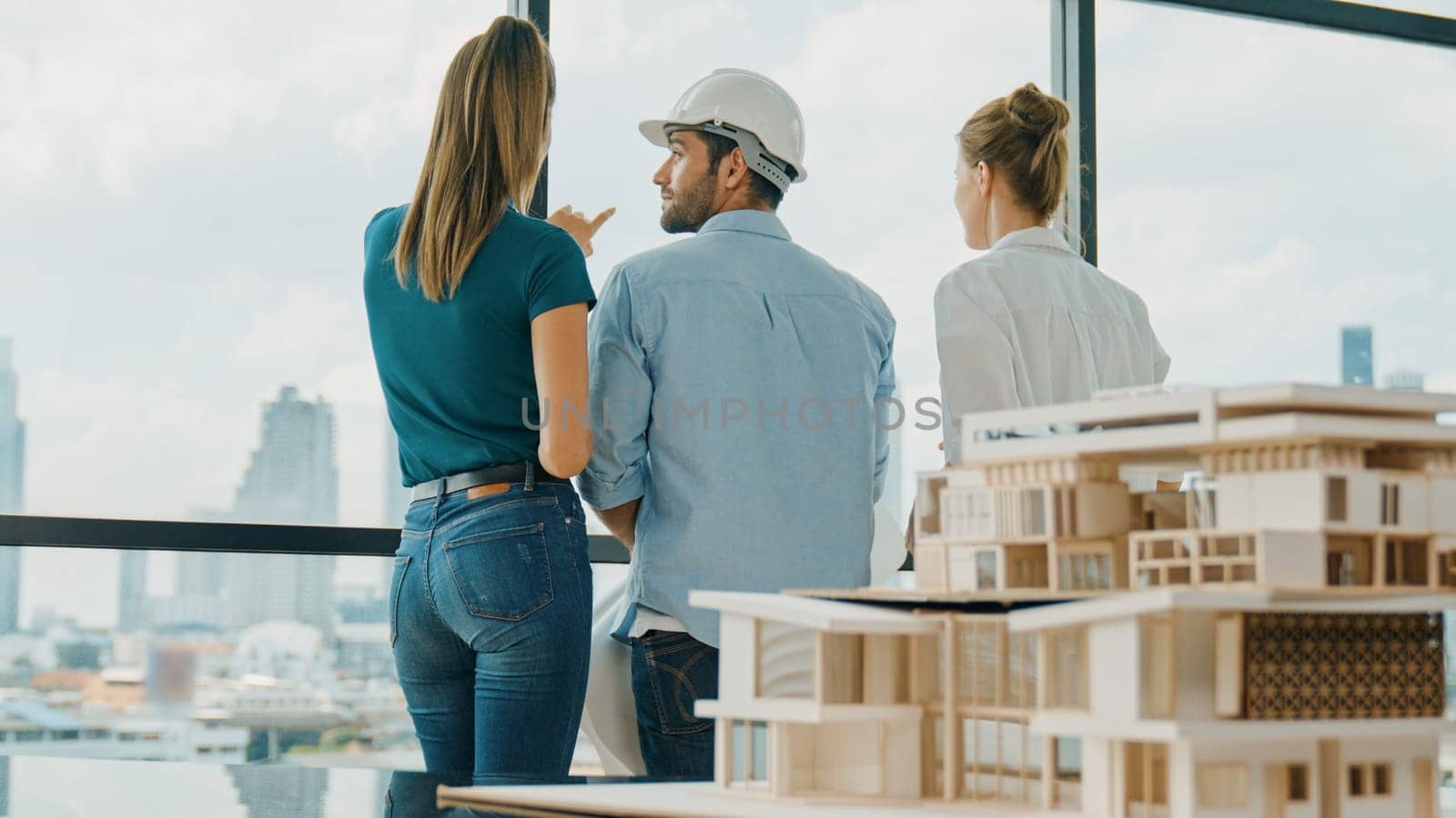 Group of caucasian diverse architect engineer pointing at skyscraper at day time. Skilled manager team looking at city or skyscraper while house model was placed on table. Back view. Tracery