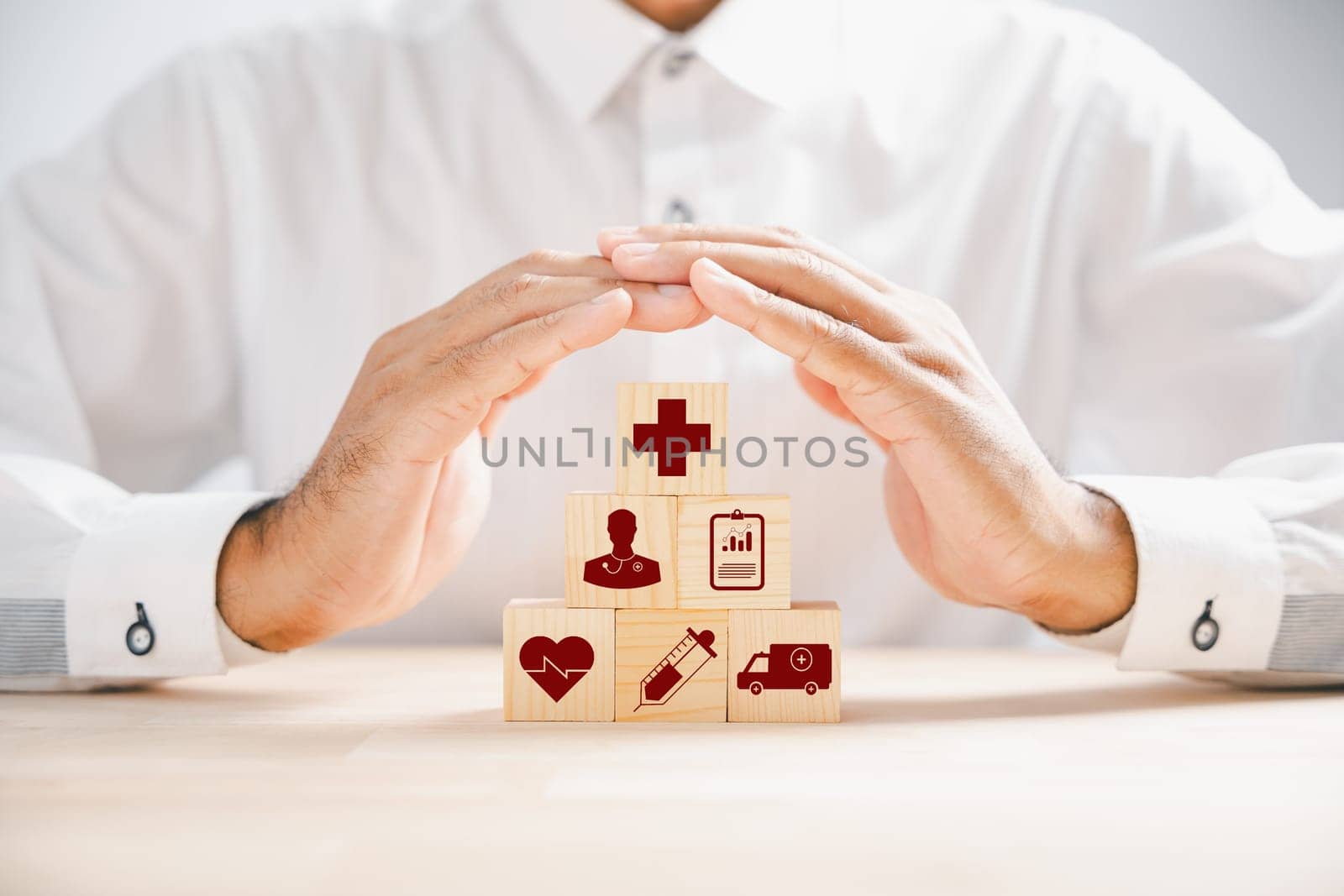 Wooden cube block displaying healthcare icons, topped by a doctor hand indicating protection, exemplifying healthcare and insurance concept. Building a secure medical future. Health care concept