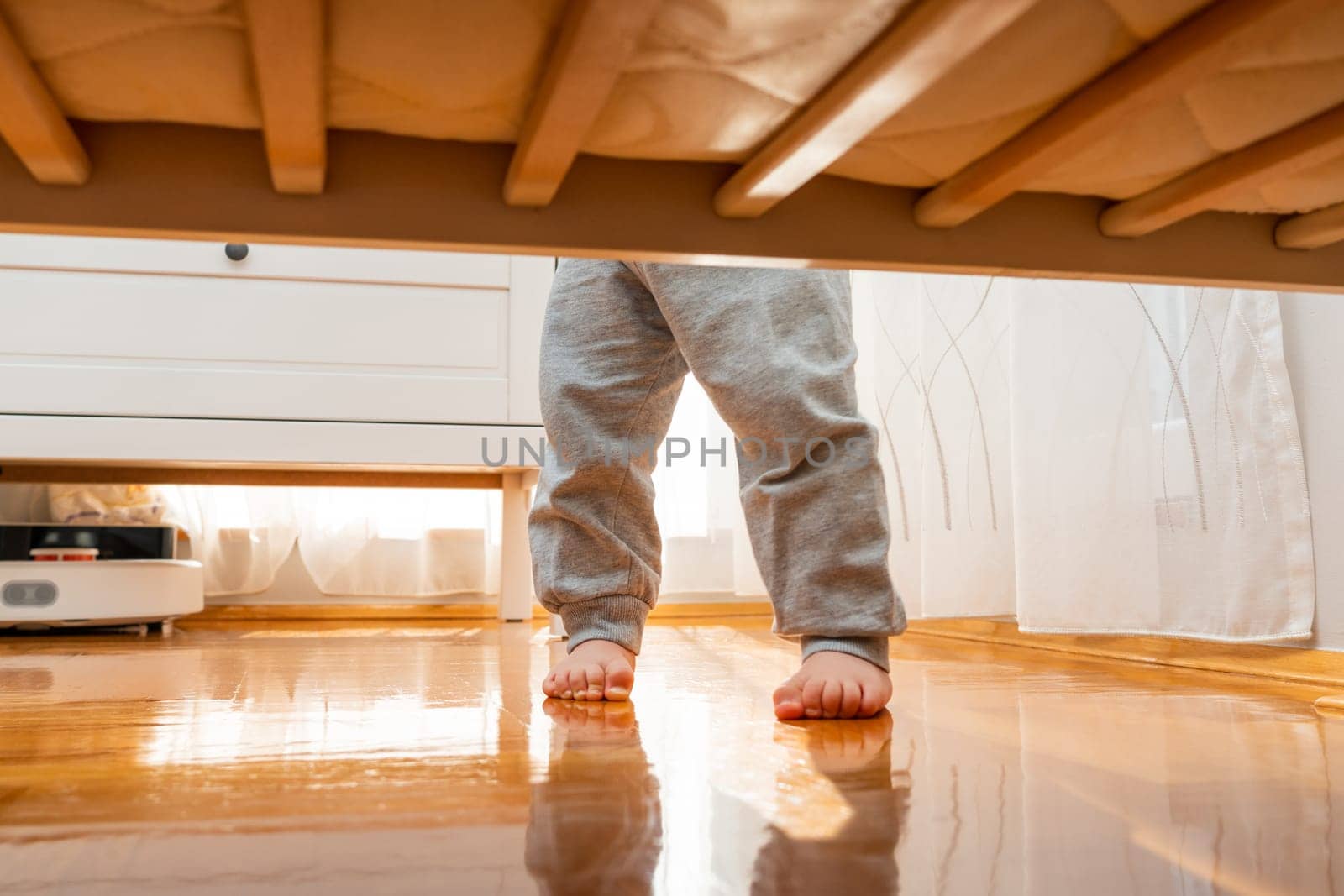 Baby standing firmly barefoot in a crib photographed from the floor. Hidden frame concept.