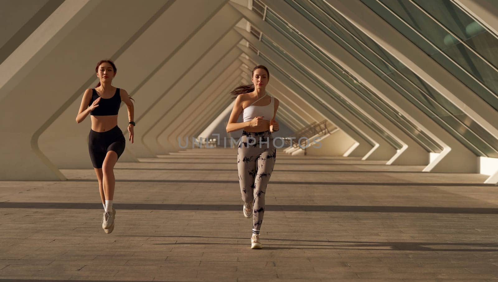 Two athletic women in sportswear is jogging around the city in early morning. Reaching the goal by Yaroslav_astakhov