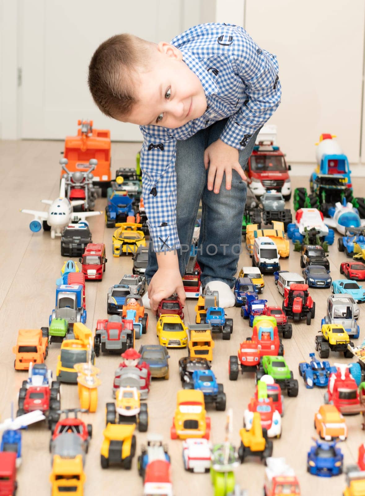 Children. Toy cars. A small cheerful and handsome boy, 4 years old, wearing a checkered shirt, plays with many colorful cars in a home interior. by ketlit