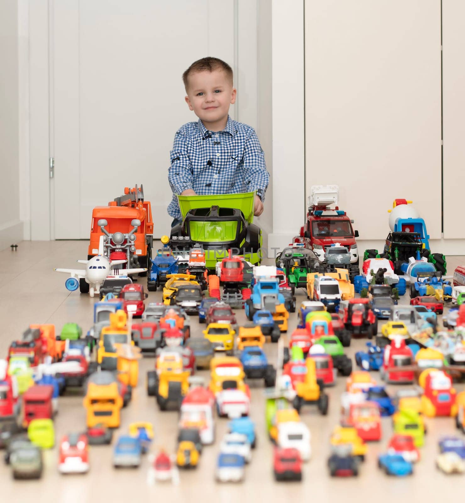 Concept of children's toys. A little boy, 4 years old, cheerful and handsome, happily plays, sitting on the floor, with multi-colored small and large cars in the children's room. Soft focus