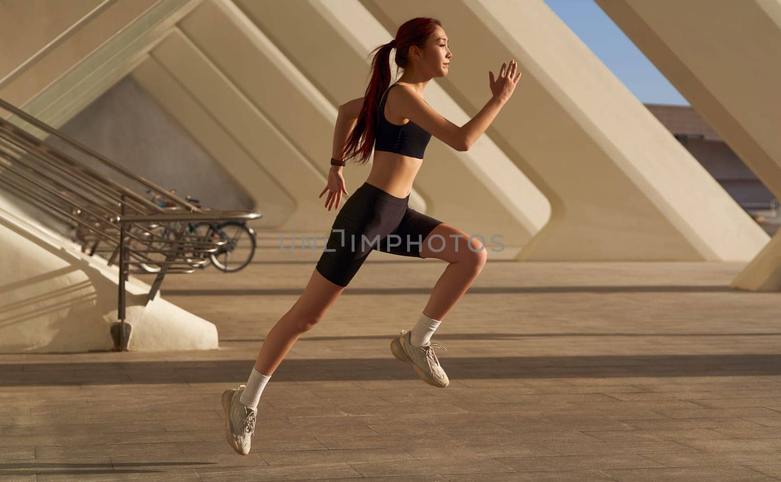 Young woman in sportswear is running on modern buildings background. Active lifestyle concept by Yaroslav_astakhov